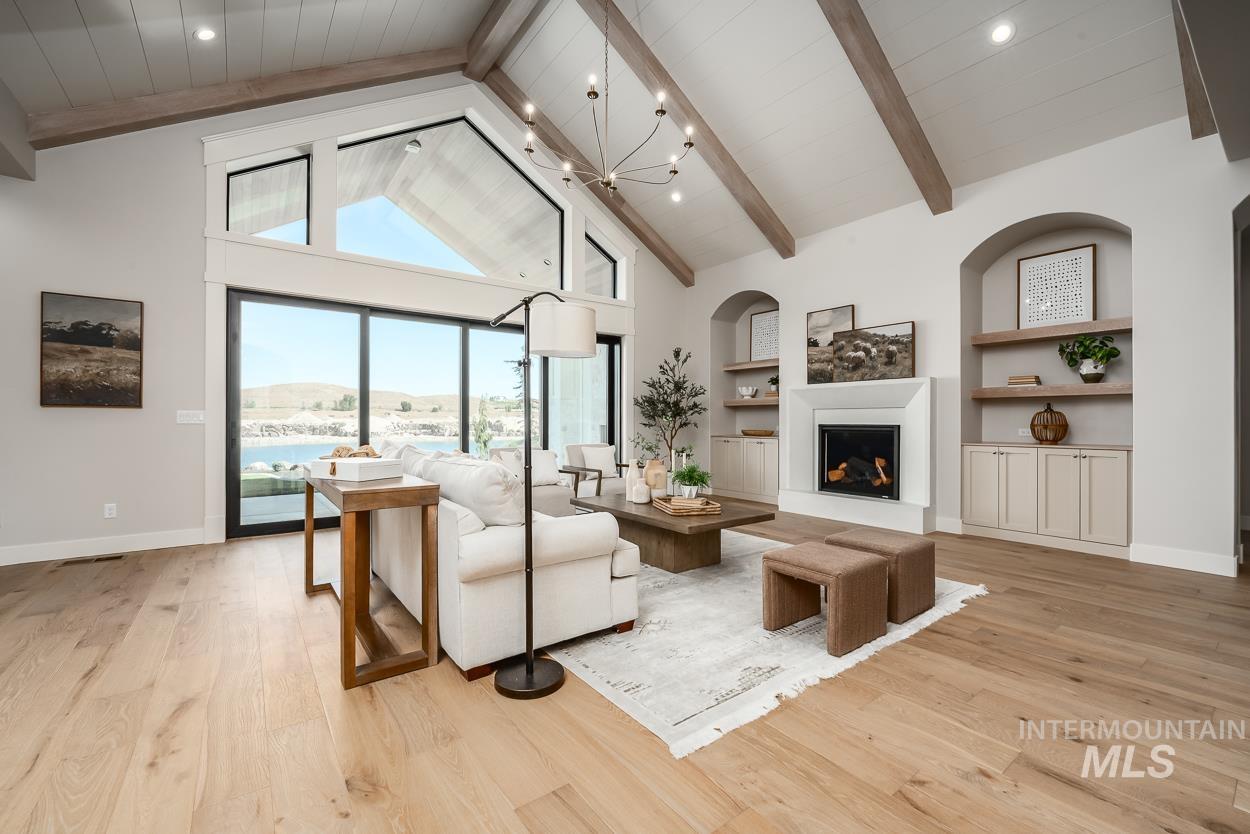 Living room featuring built in shelves, high vaulted ceiling, a chandelier, light wood finished floors, and a fireplace with raised hearth