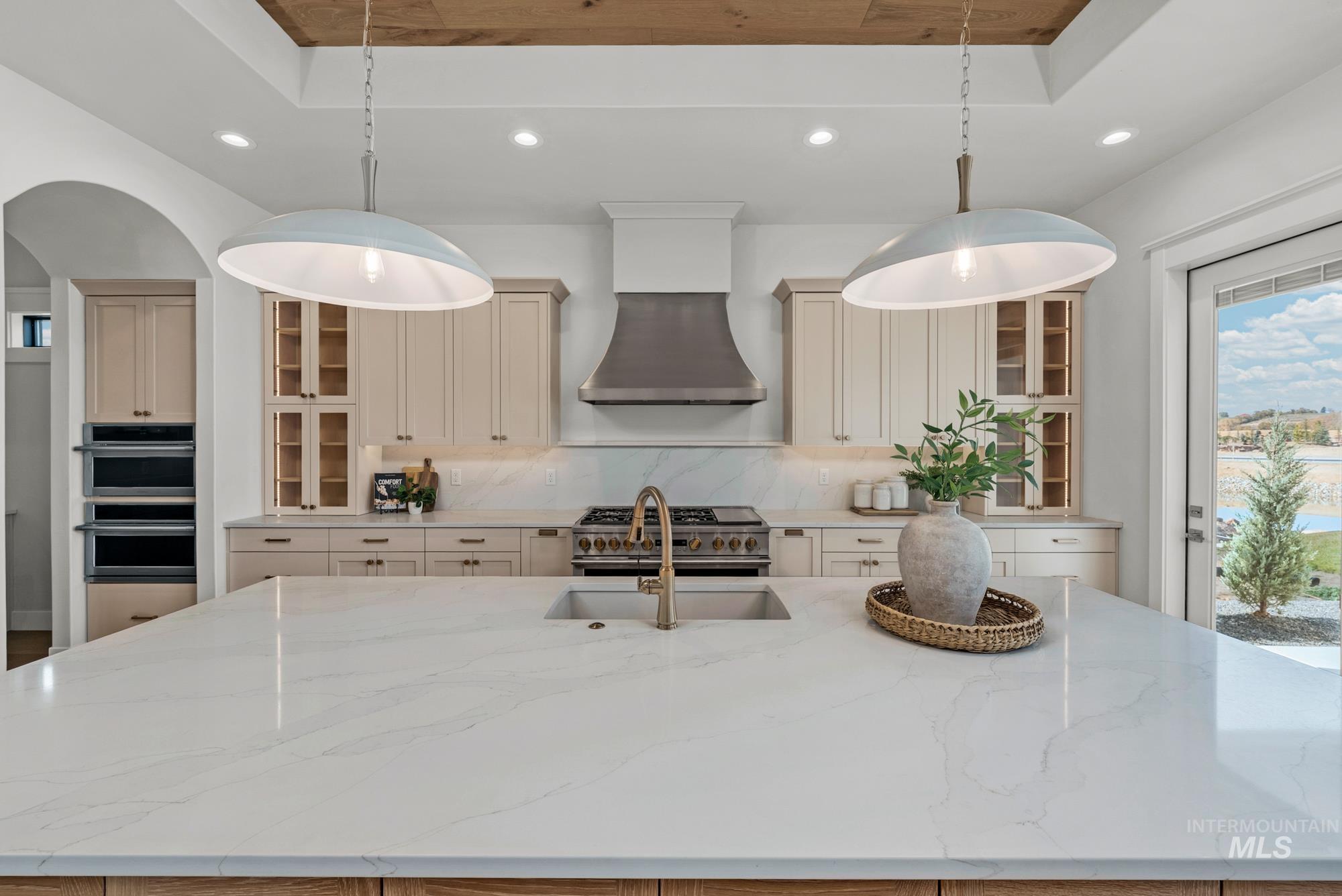 Kitchen featuring glass insert cabinets, recessed lighting, a center island with sink, light stone counters, and decorative backsplash
