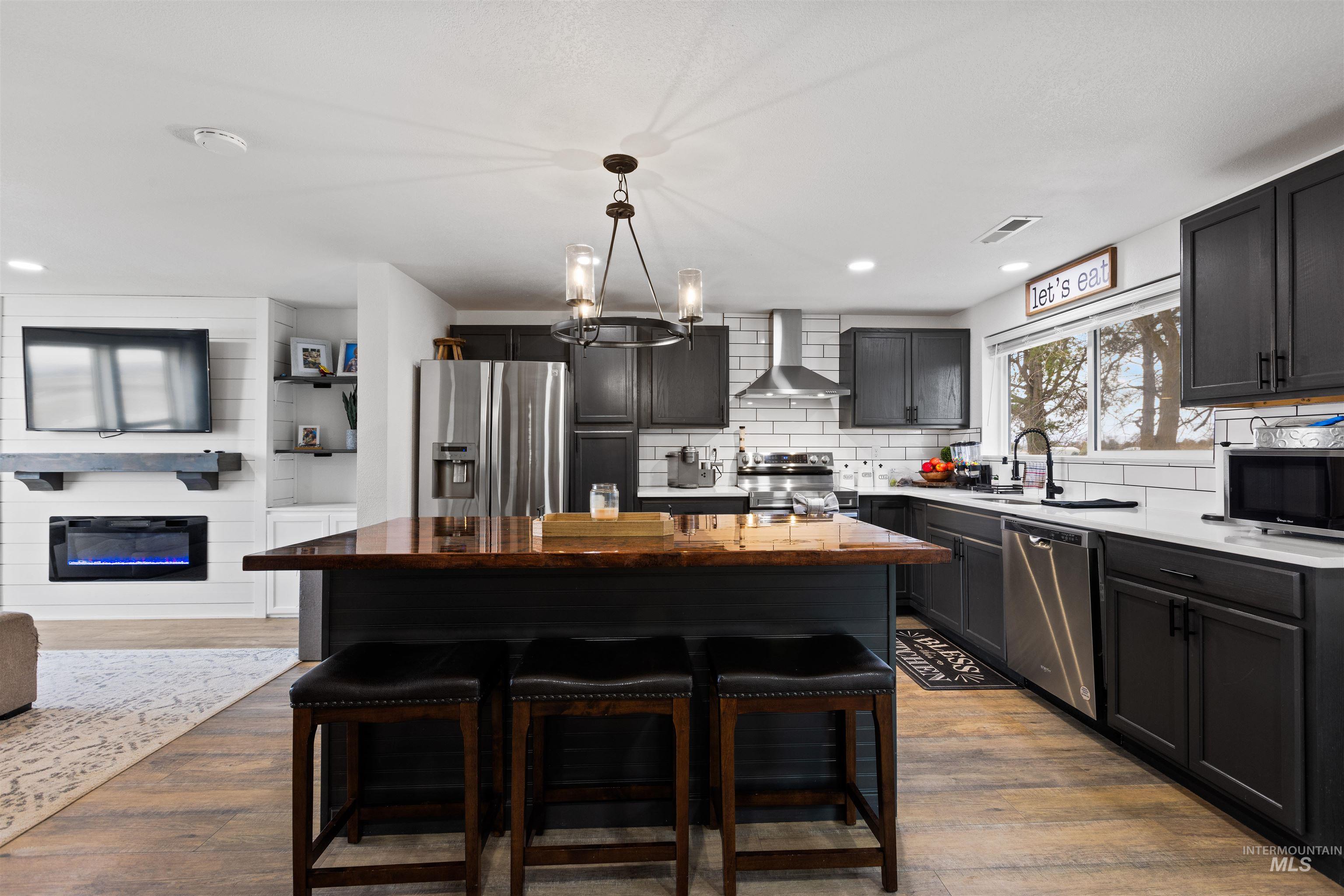 Kitchen with a kitchen breakfast bar, a large fireplace, stainless steel appliances, suspended lighting, and light wood-type flooring