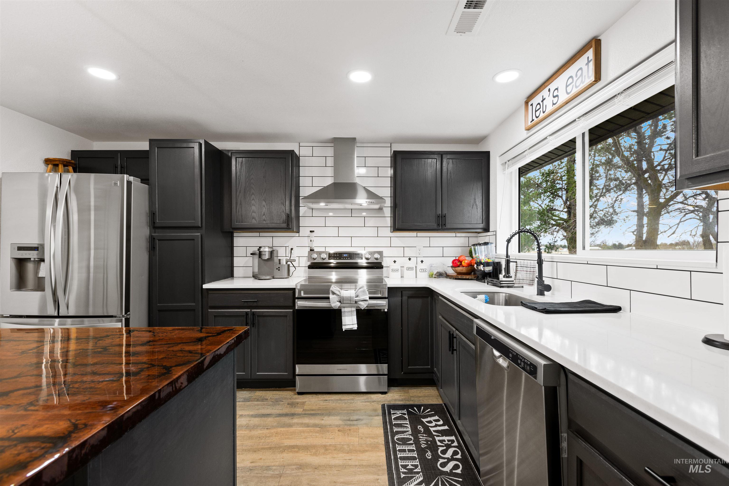 Kitchen featuring stainless steel appliances, range hood, decorative backsplash, dark stone countertops, and recessed lighting