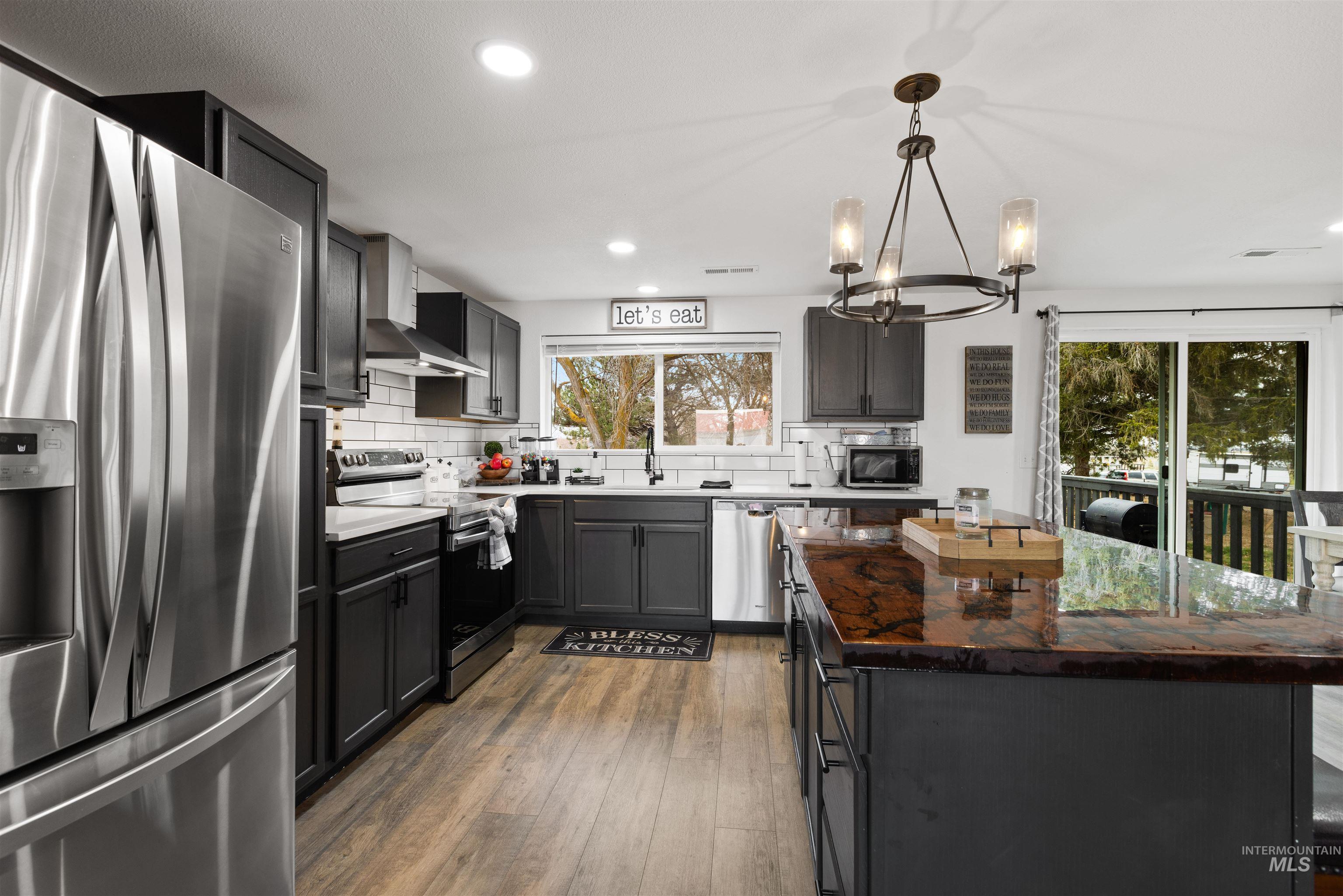 Two tone kitchen featuring stainless steel appliances, dark wood-style flooring, a center island, suspended lighting, and backsplash