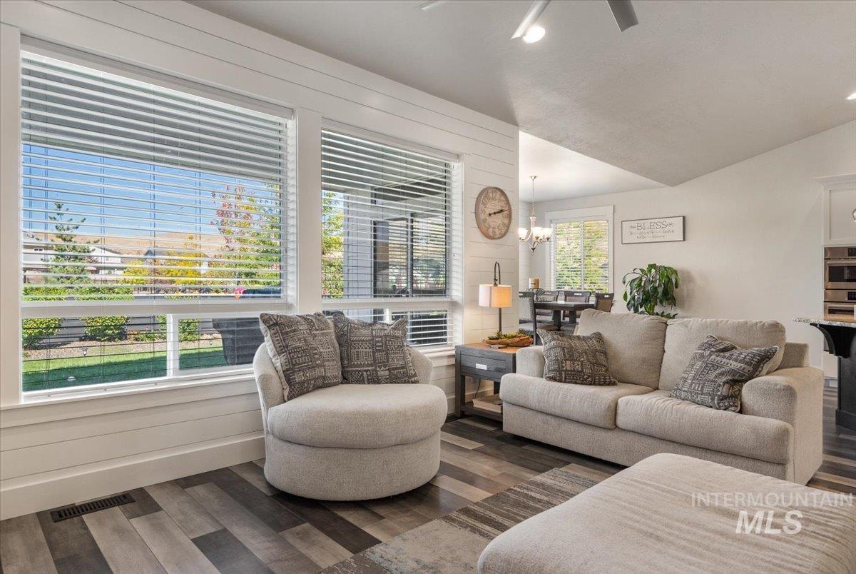 Living room featuring wood finished floors, a chandelier, a ceiling fan, and lofted ceiling