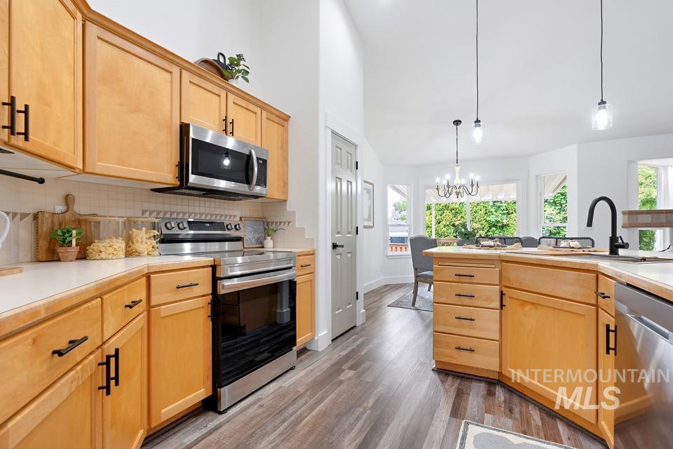 Kitchen with light brown cabinets, appliances with stainless steel finishes, light countertops, hanging light fixtures, and dark wood-type flooring