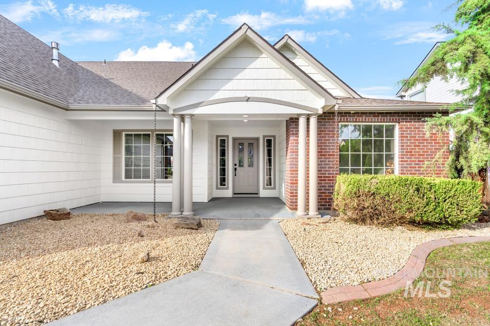 Property entrance featuring brick siding, covered porch, and roof with shingles