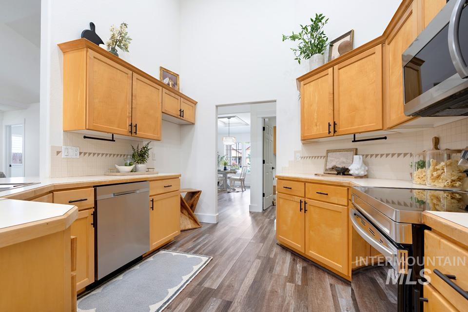 Kitchen with tasteful backsplash, appliances with stainless steel finishes, light countertops, dark wood-style flooring, and a high ceiling