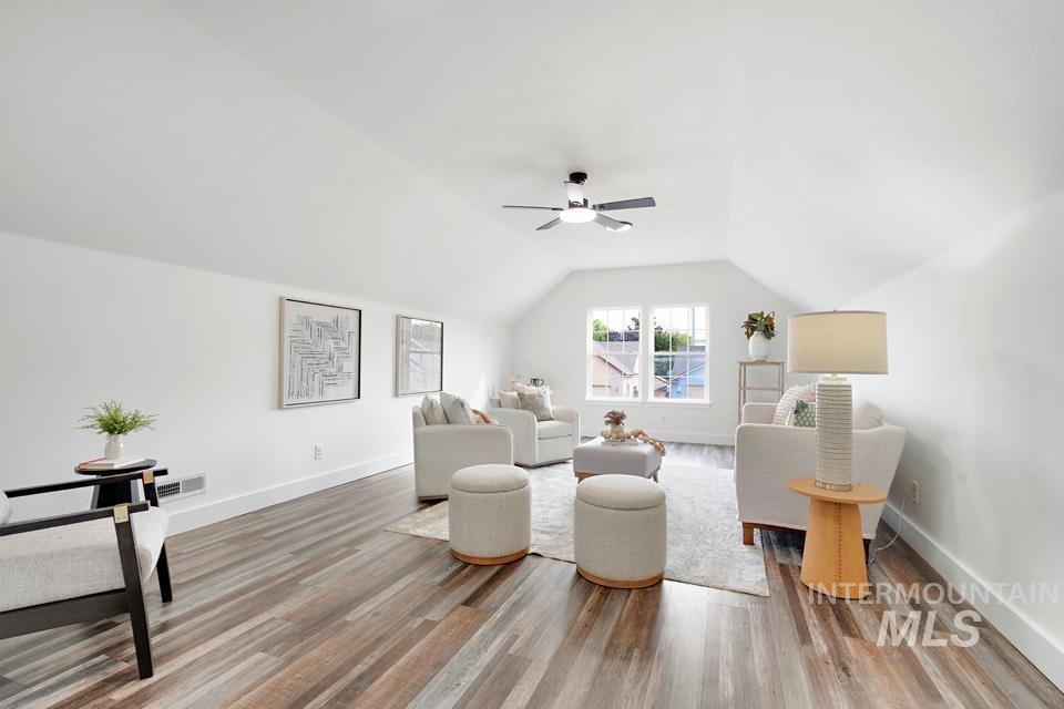 Living area featuring vaulted ceiling, light wood-style floors, and ceiling fan