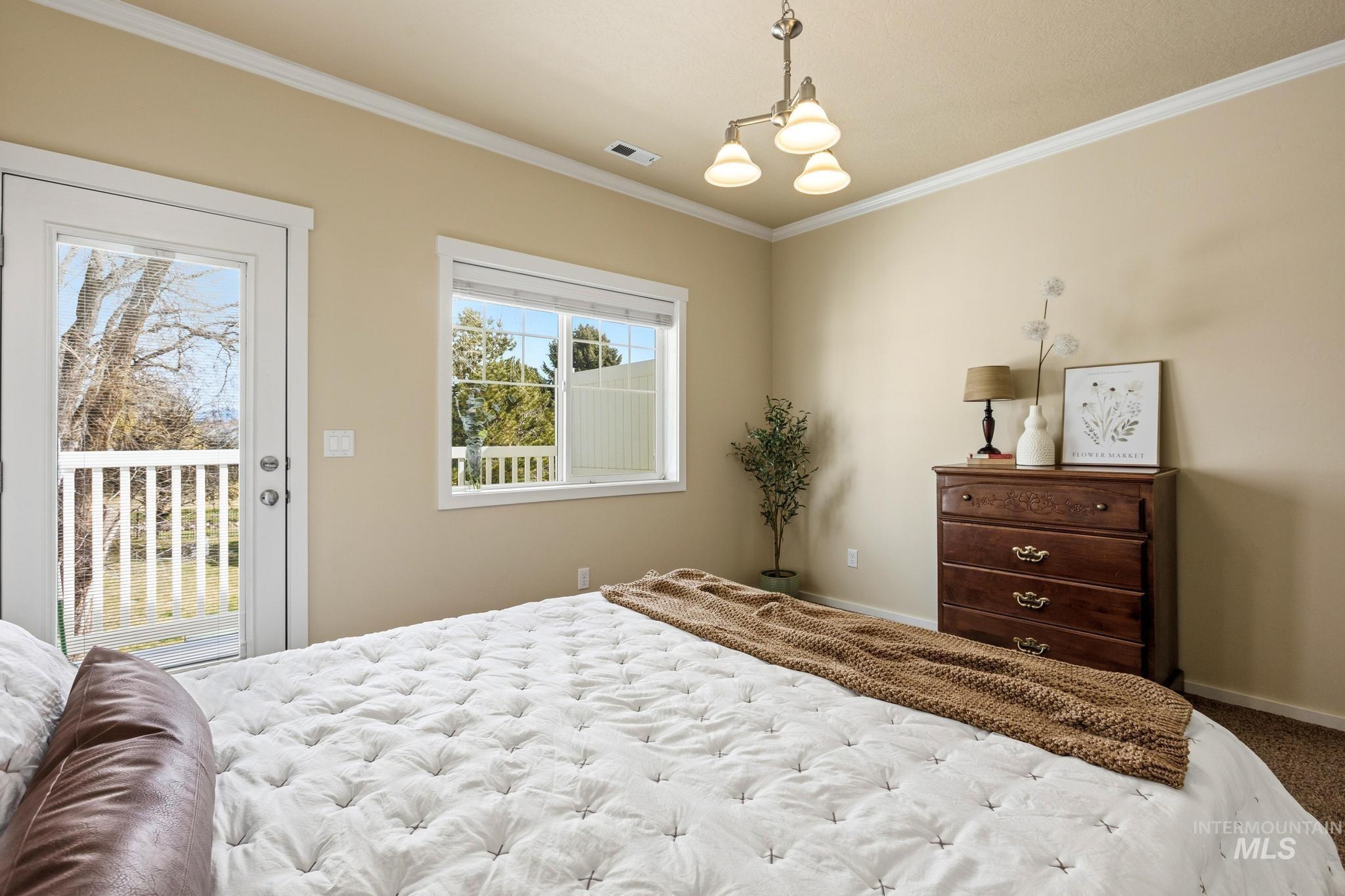 Bedroom with ornamental molding, access to exterior, hanging lights, and carpet