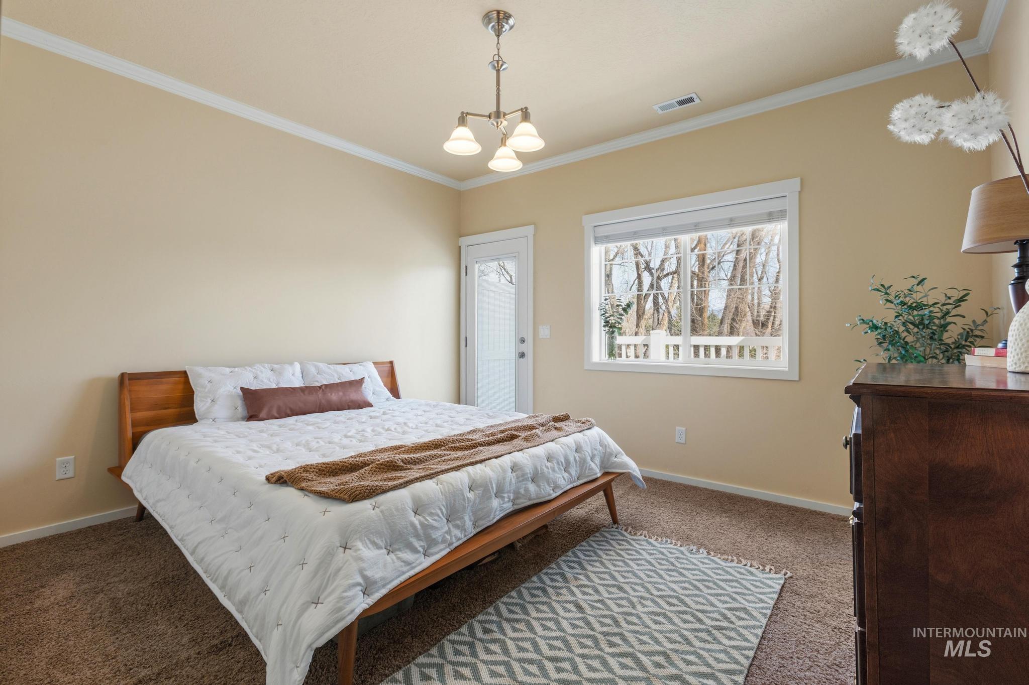 Bedroom with hanging lights, ornamental molding, and light colored carpet