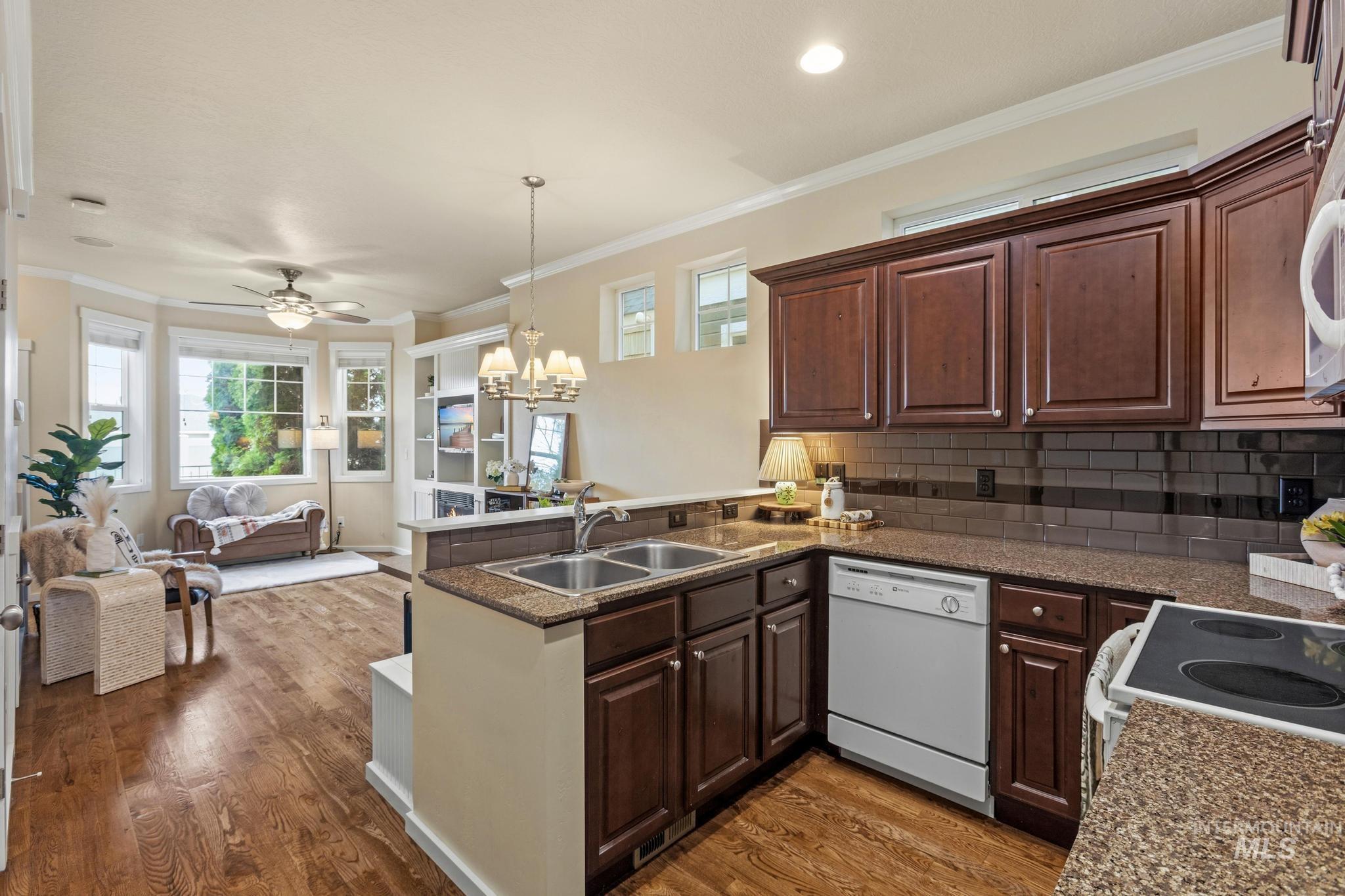 Kitchen featuring a peninsula, a chandelier, open floor plan, crown molding, and white appliances