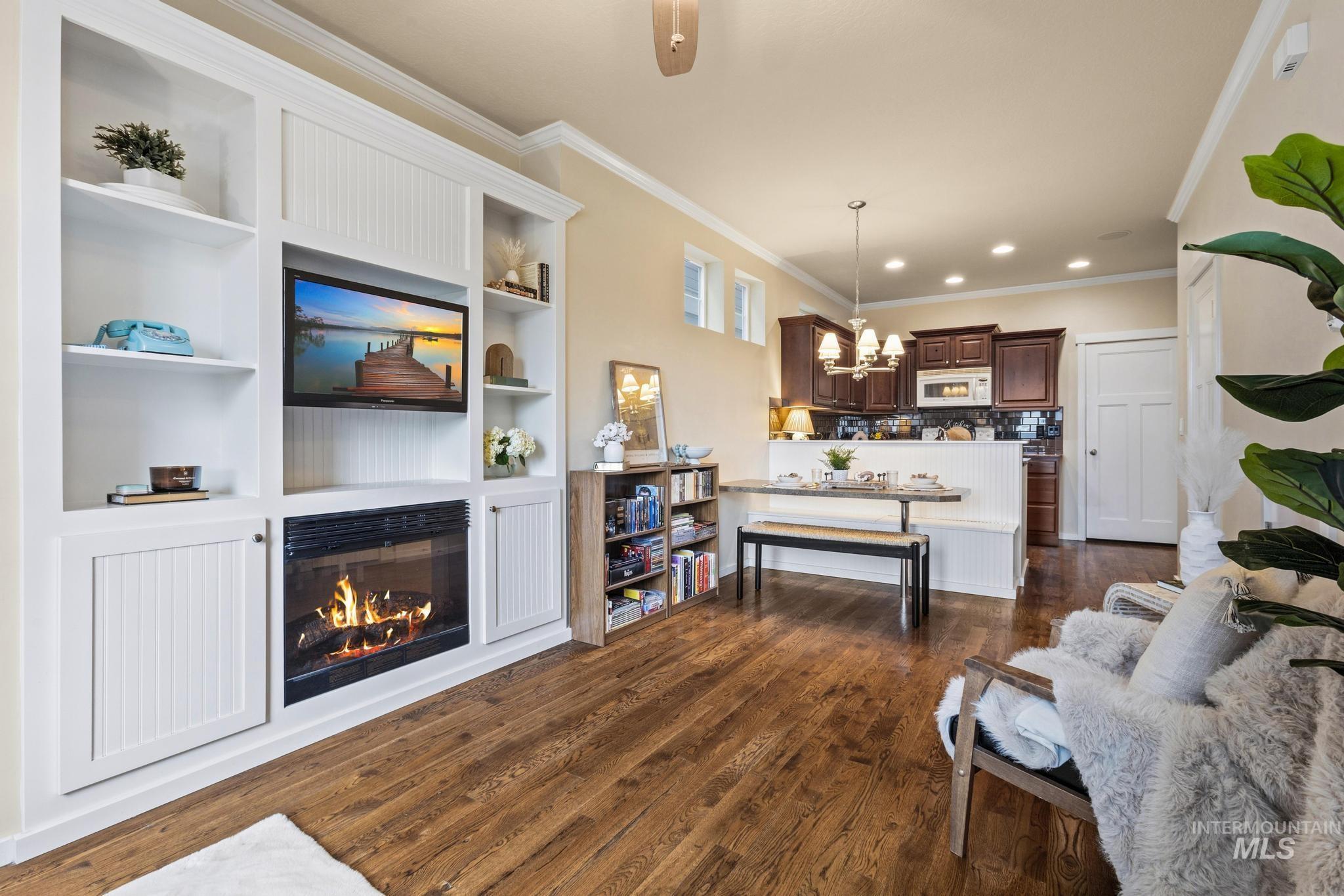 Living area featuring a glass covered fireplace, ornamental molding, dark wood-type flooring, built in features, and a chandelier