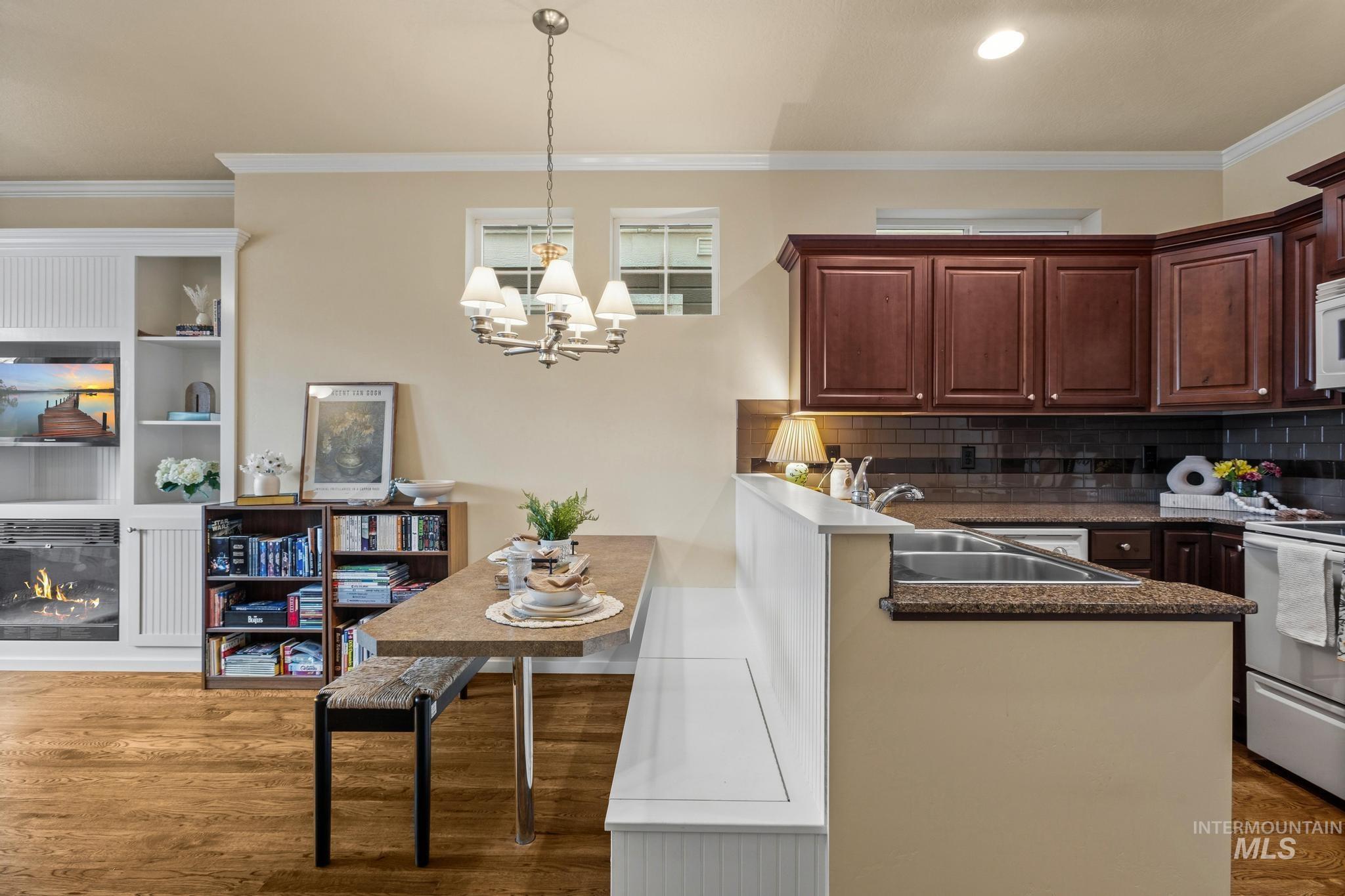 Kitchen featuring ornamental molding, a kitchen breakfast bar, white appliances, a peninsula, and a glass covered fireplace