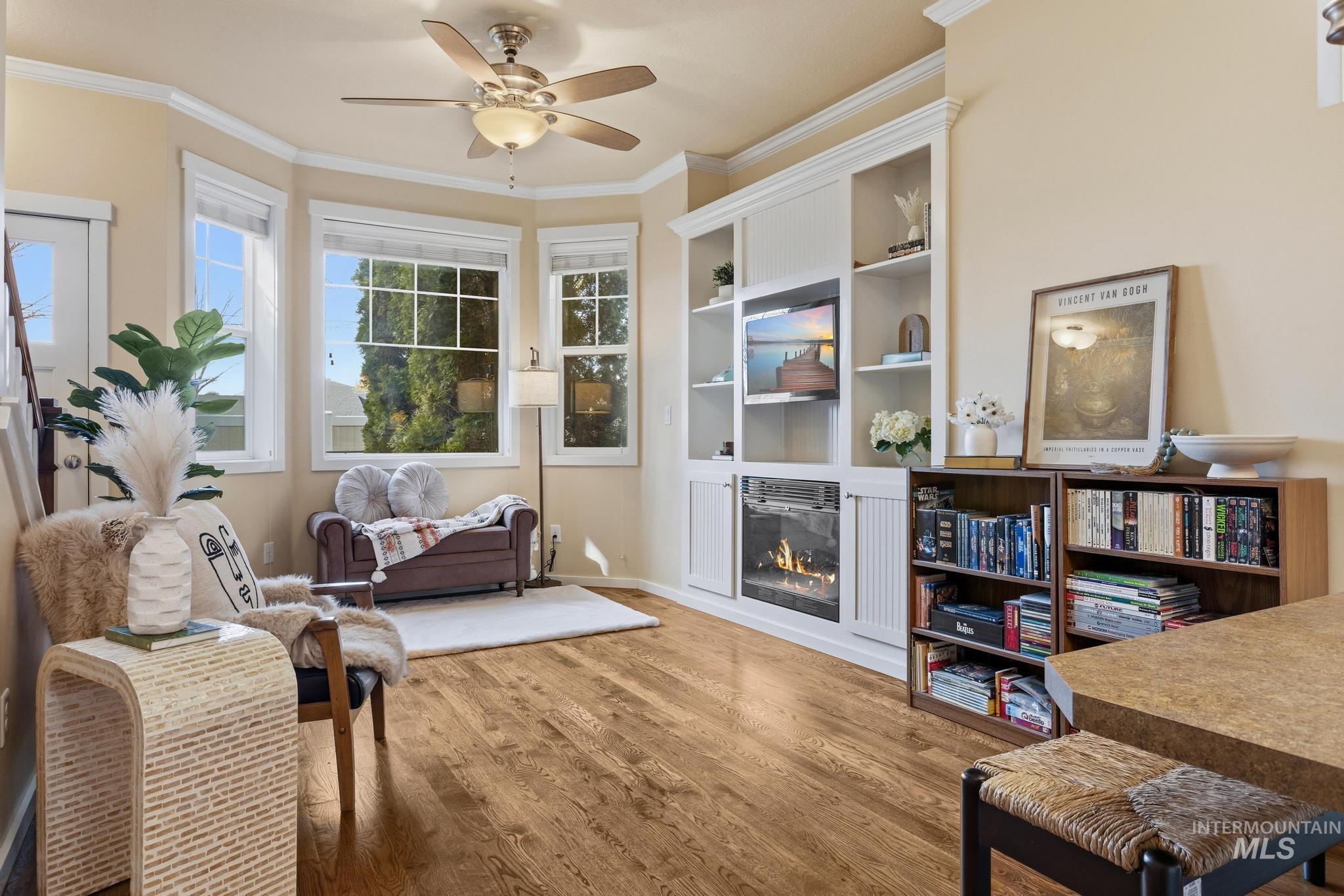 Living area with ornamental molding, a glass covered fireplace, light wood finished floors, a ceiling fan, and built in features