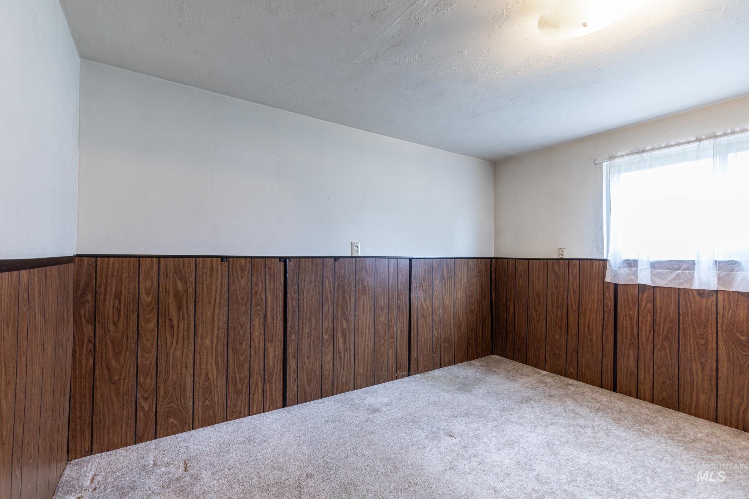 Unfurnished room with wooden walls, carpet flooring, wainscoting, and a textured ceiling