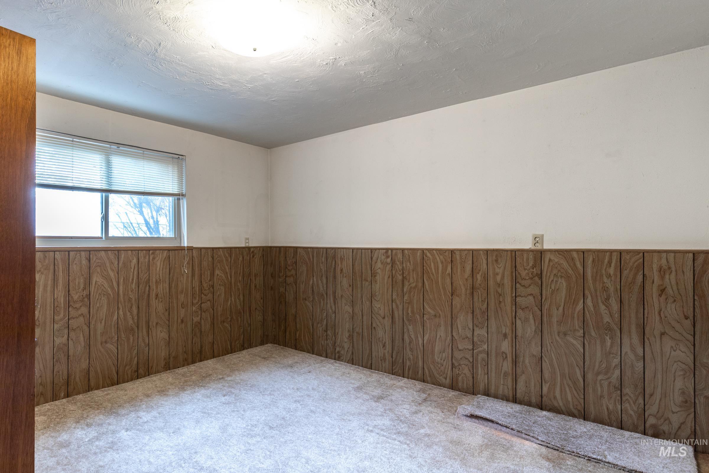 Carpeted spare room with wood walls, wainscoting, and a textured ceiling