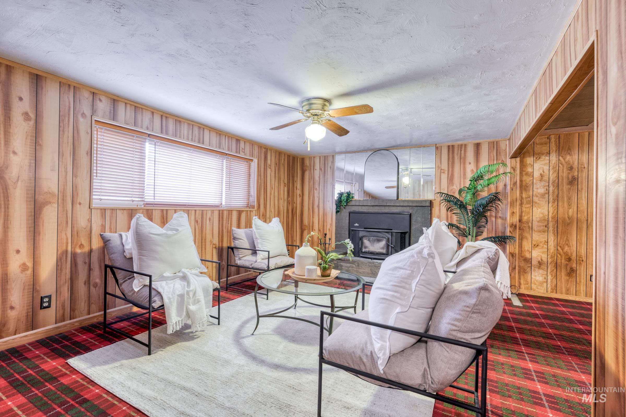 Living room with wooden walls, ceiling fan, a textured ceiling, and a wood stove