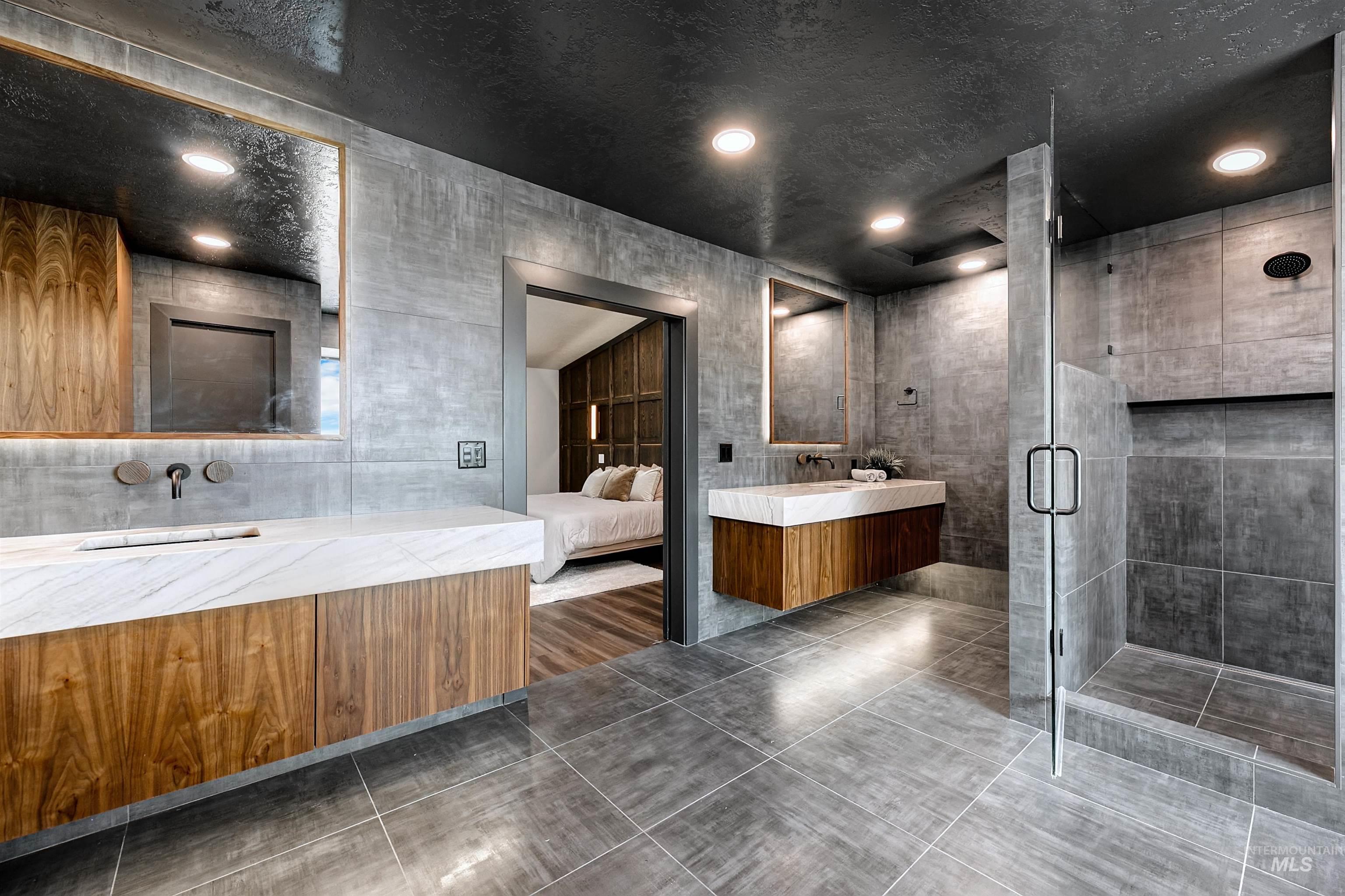 Master bathroom featuring a tiled shower, dual vanities, tile walls, recessed lighting, and dark tile patterned floors.