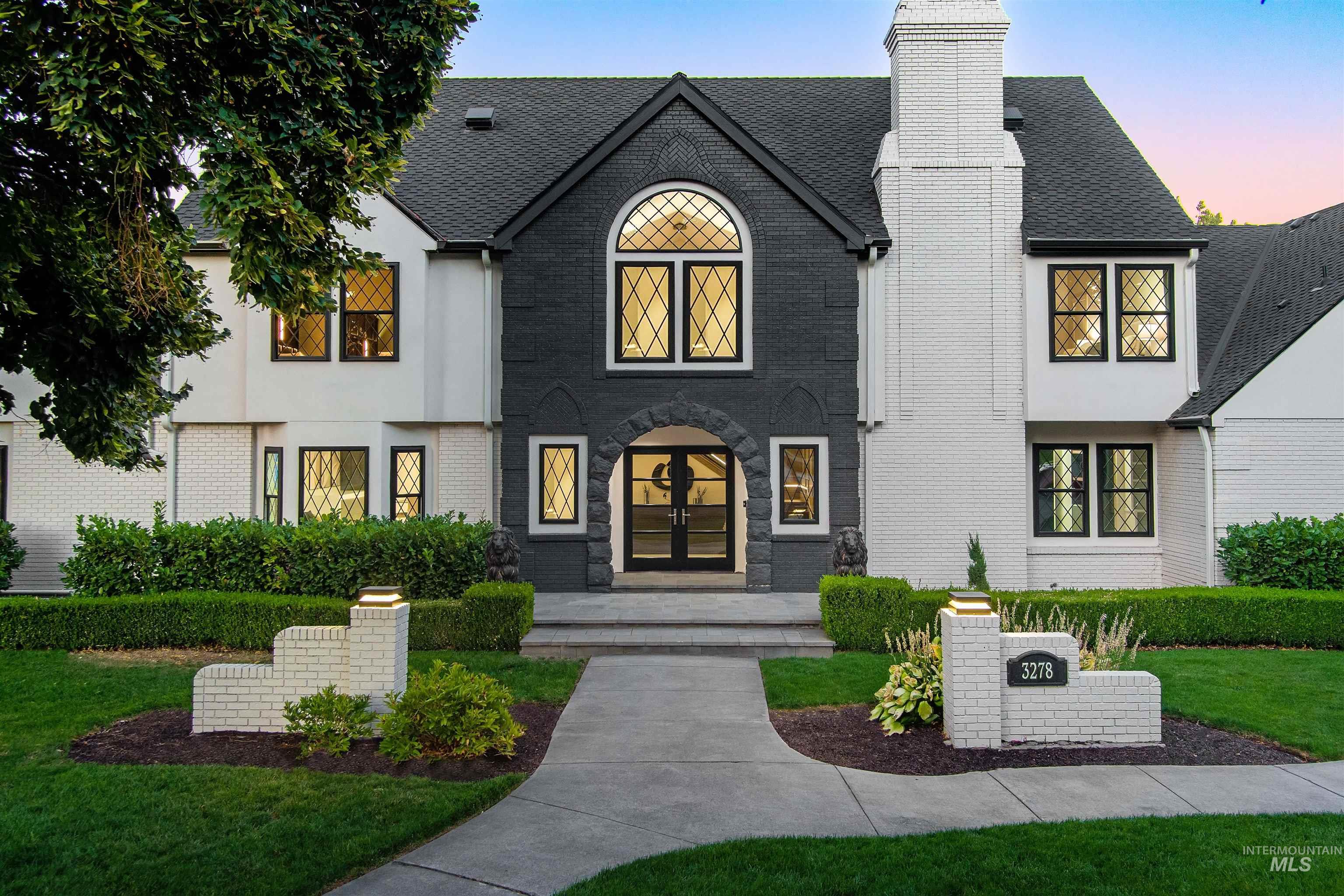View of front of house featuring brick and stucco, green lawn, french doors, and a shingled roof.
