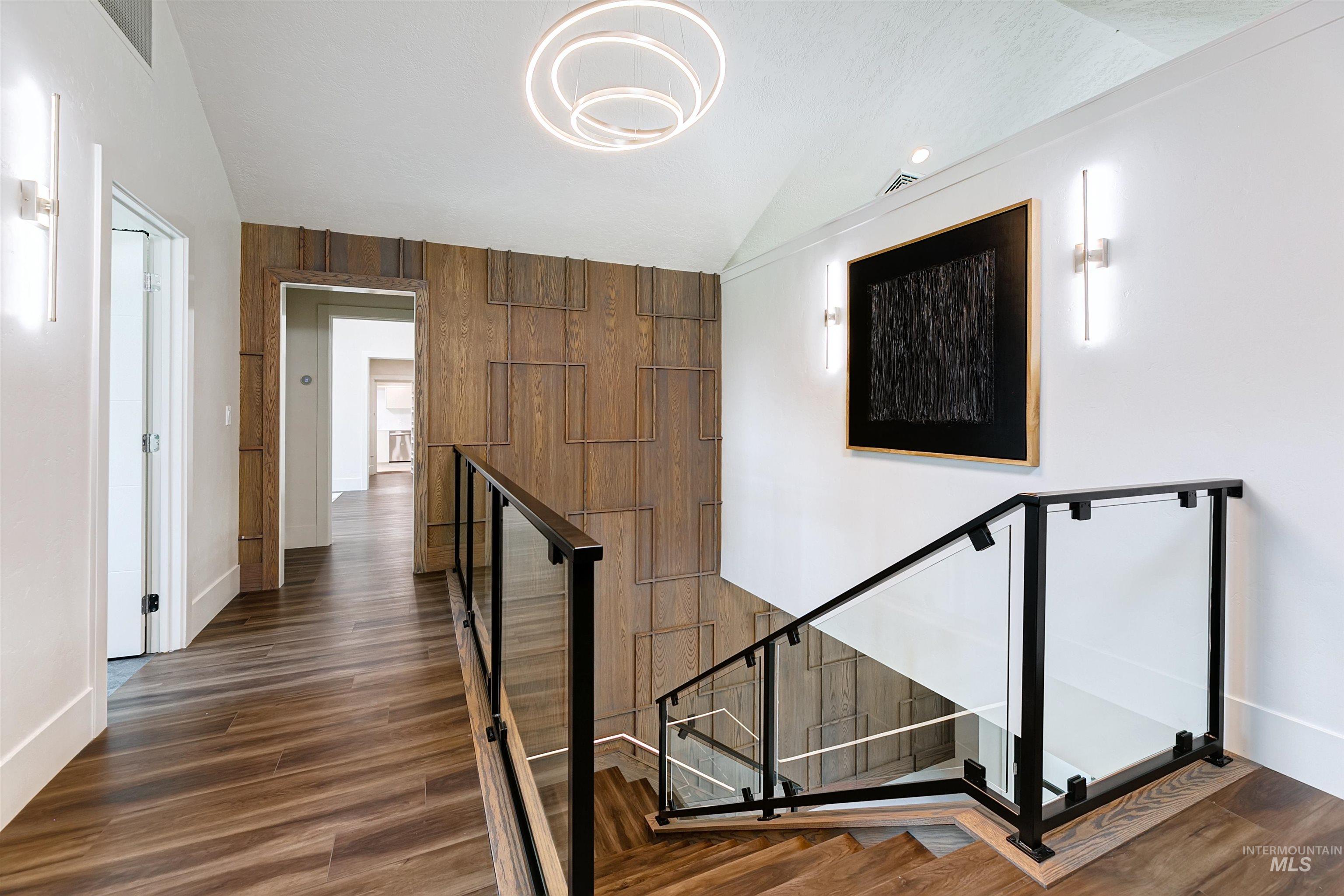 Stairs with a designer light fixture, finished floors, and wooden wall accents.