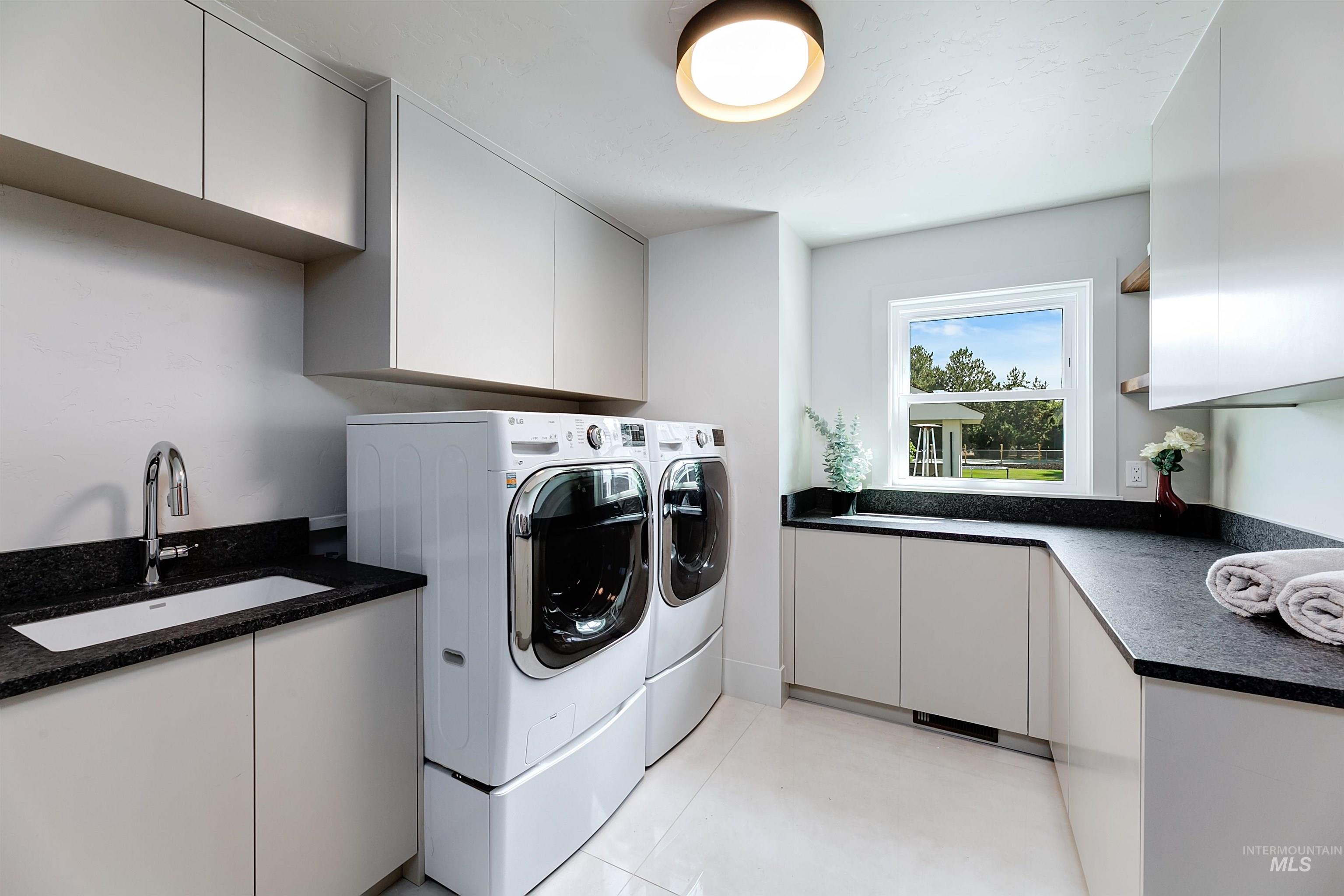 Main level laundry room with cabinet space, light tile patterned floors, and washer and dryer units.