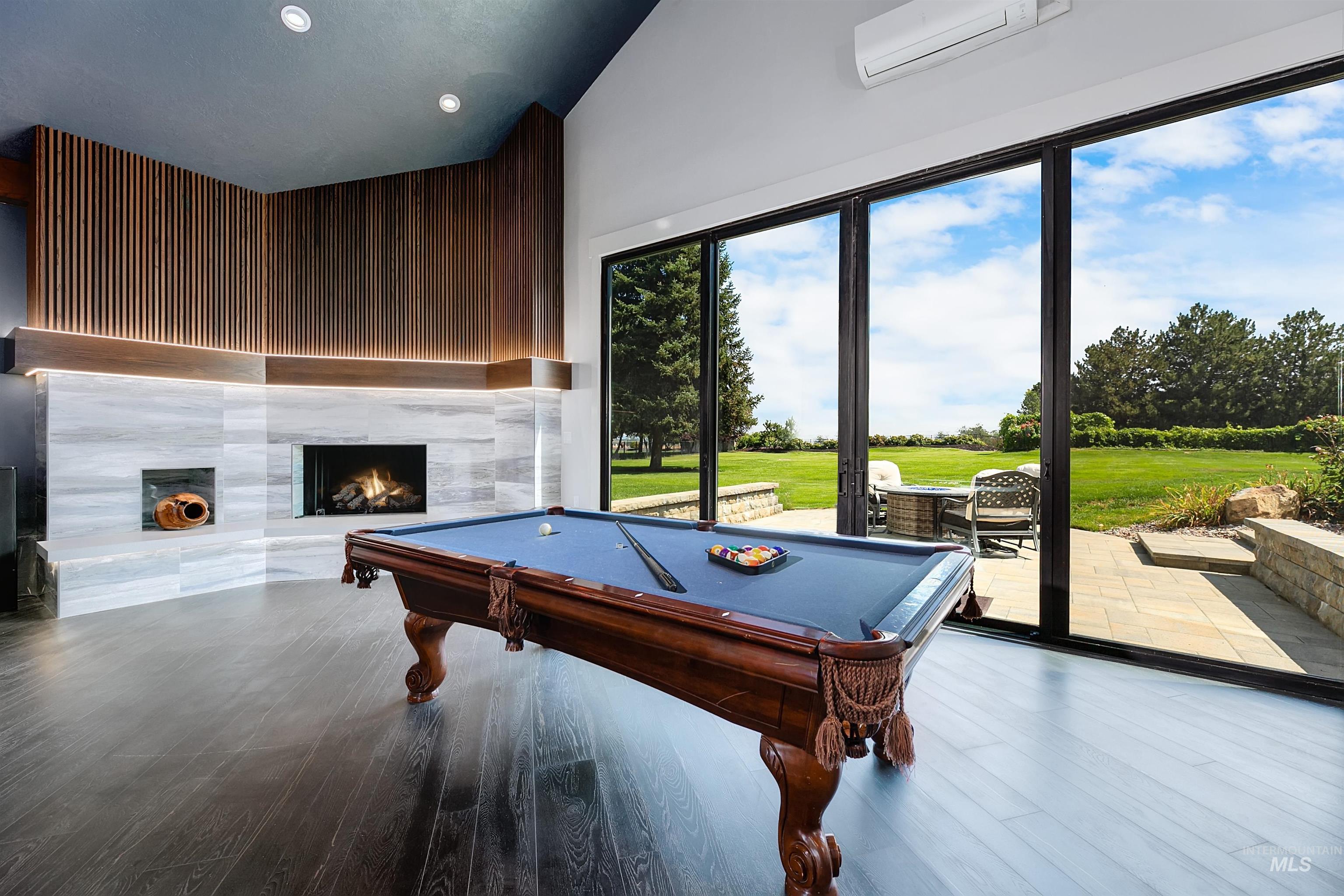 Great room featuring billiards table, a tiled fireplace, wood finished floors, vaulted ceiling, and a wall unit AC.