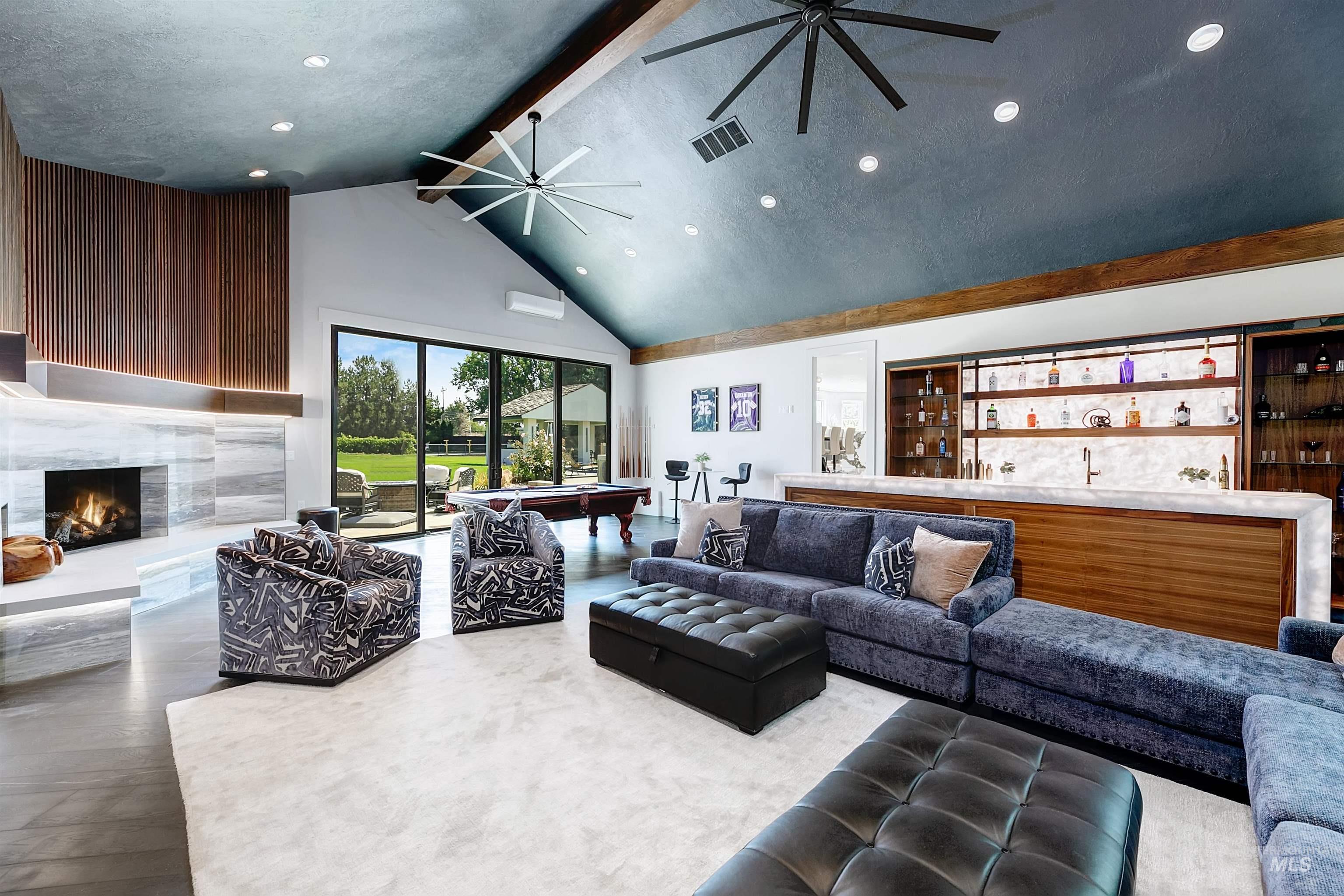 Great room featuring beam ceiling, two ceiling fans, a high end fireplace, billiards table, wine bar, and high vaulted ceiling.