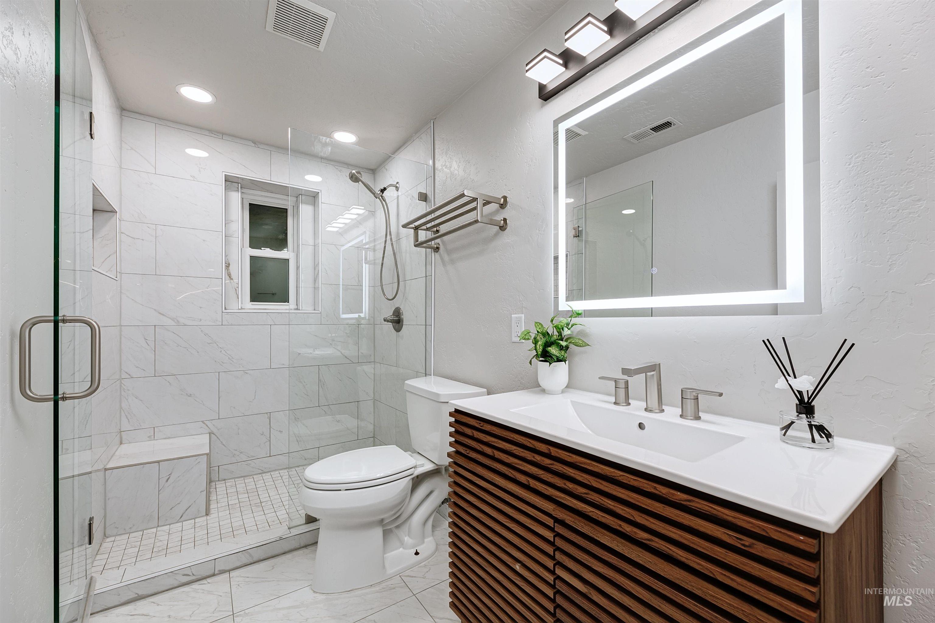 Bathroom featuring a tiled shower, vanity, and light marble finish floors.