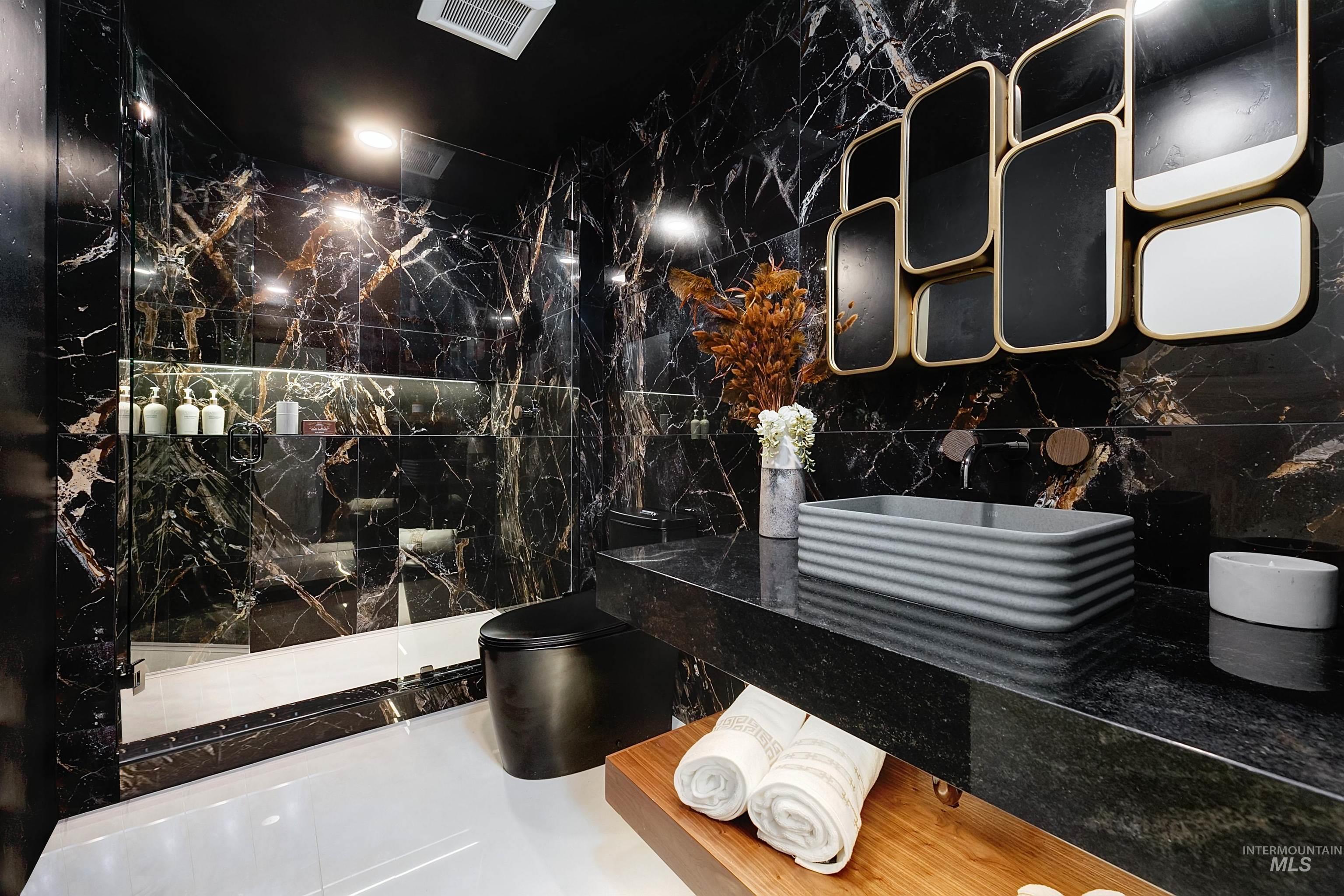 Main level full bathroom with marble tile walls, a marble finish shower, and tile patterned floors.