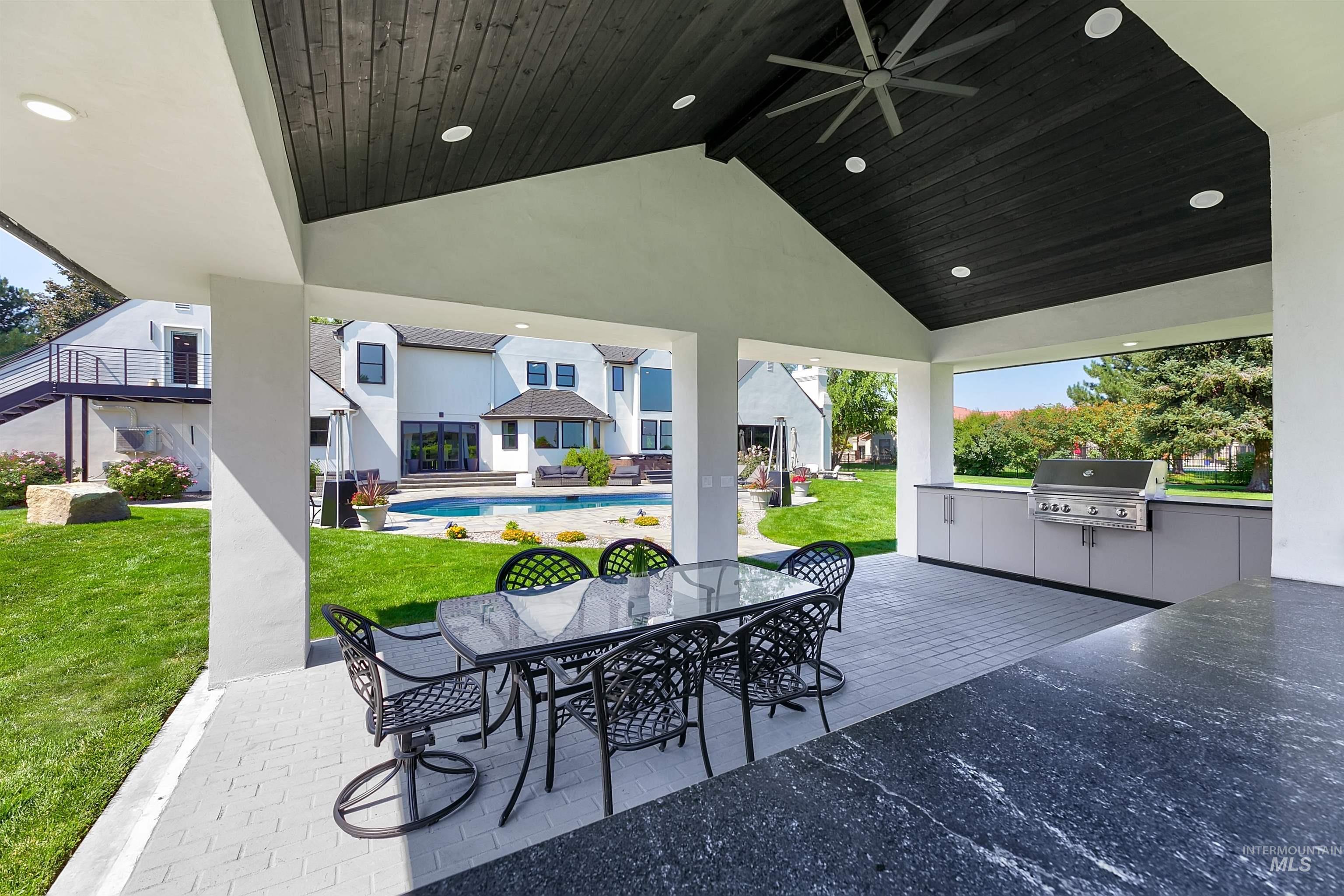 View of cabana featuring an outdoor kitchen with built-in BBQ, outdoor dining space, ceiling fan, and outdoor sound system.