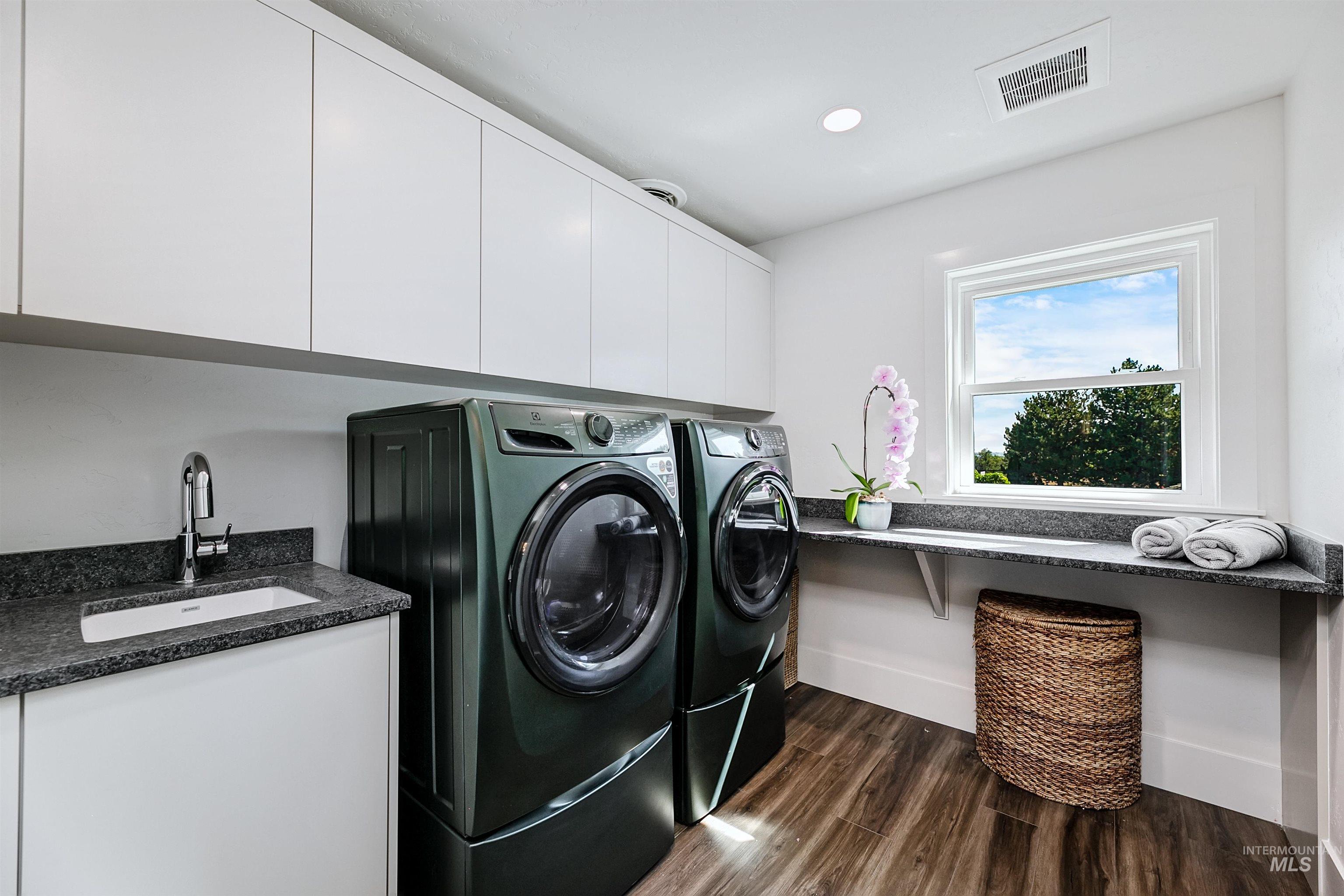 Upper level laundry room featuring dark wood-style flooring, washer and dryer, recessed lighting, and cabinet space.