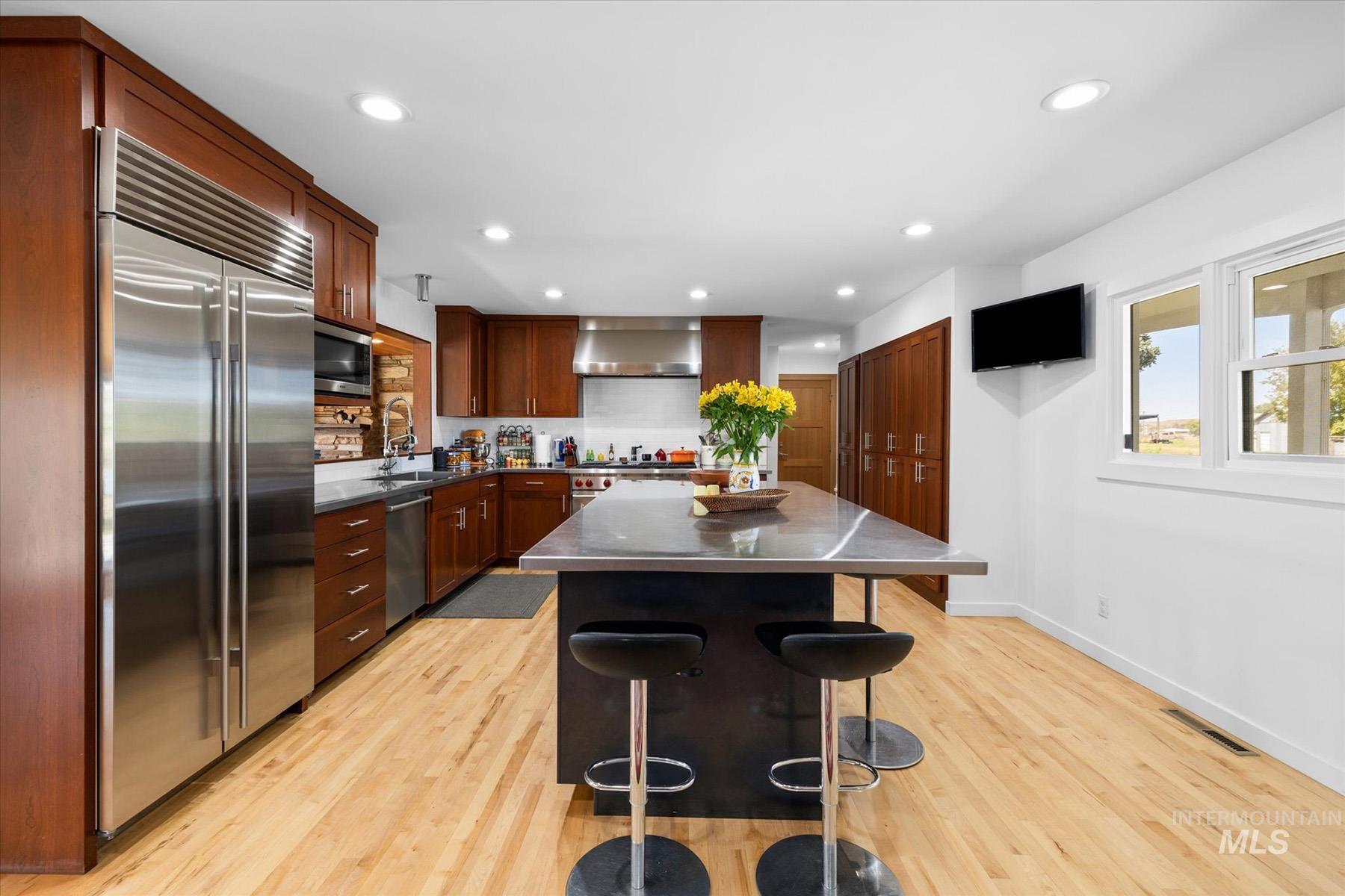 Kitchen with appliances with stainless steel finishes, wall chimney exhaust hood, light wood-style floors, a breakfast bar area, and recessed lighting