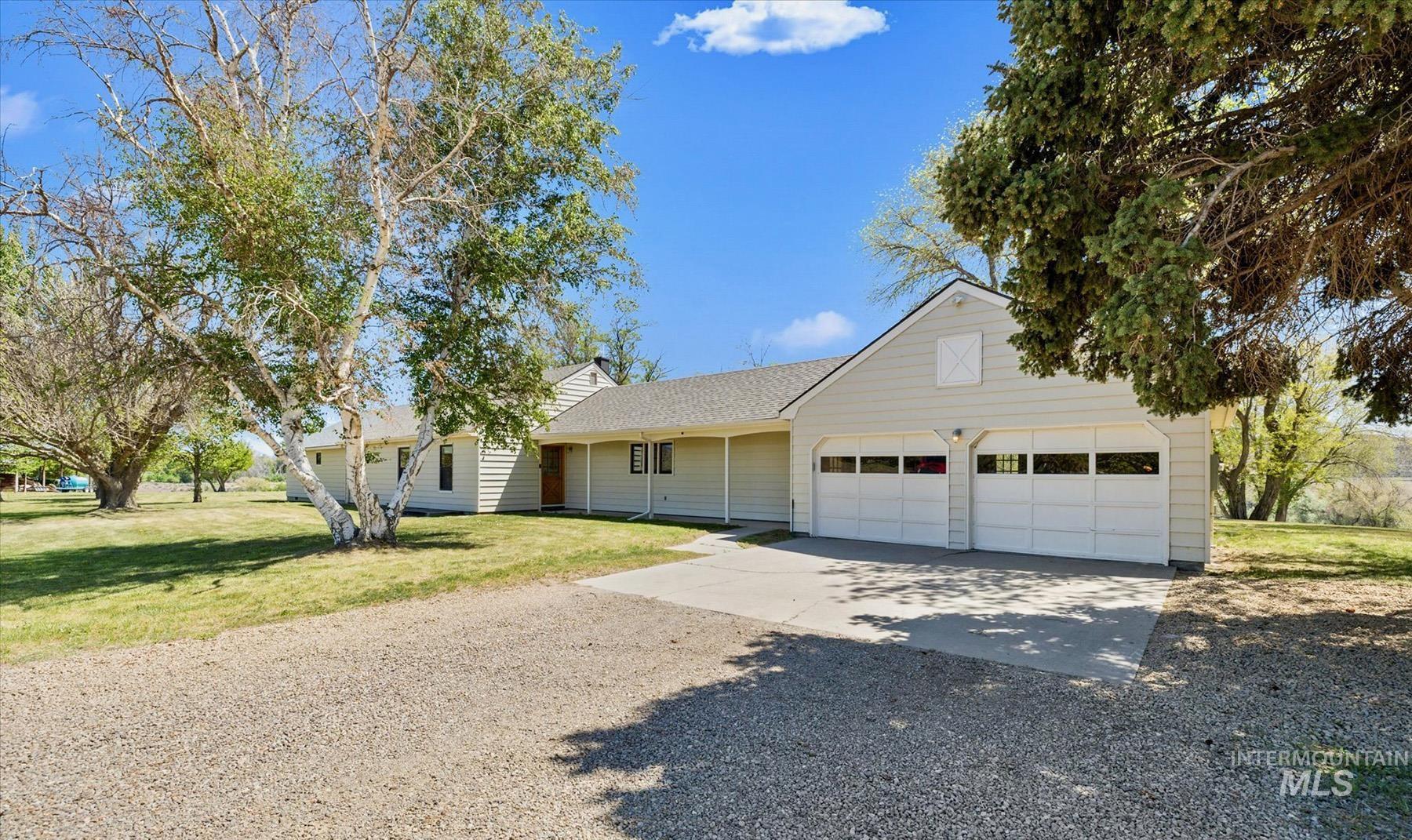 View of front of property featuring gravel driveway, an attached garage, and a front lawn