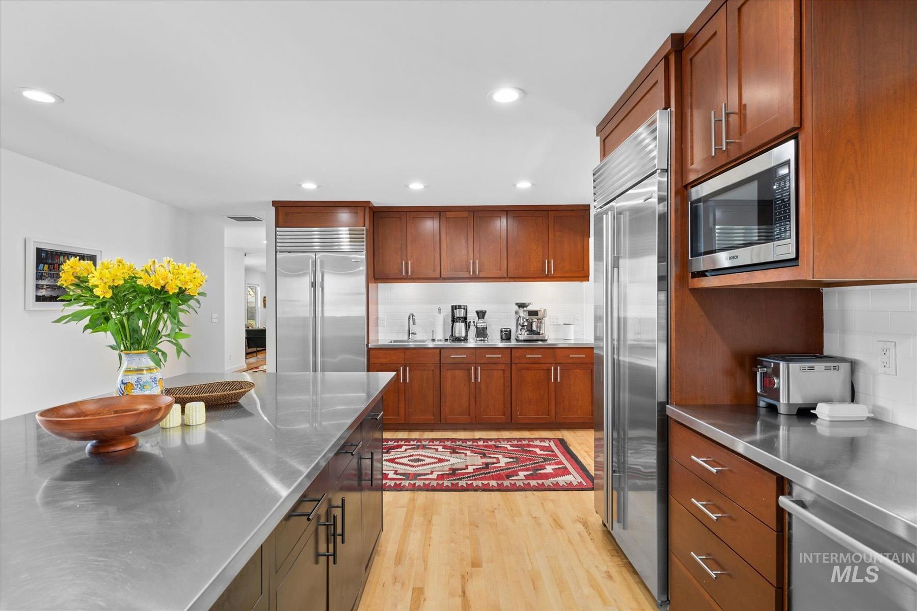 Kitchen featuring stainless steel counters, appliances with stainless steel finishes, light wood-style flooring, recessed lighting, and brown cabinetry
