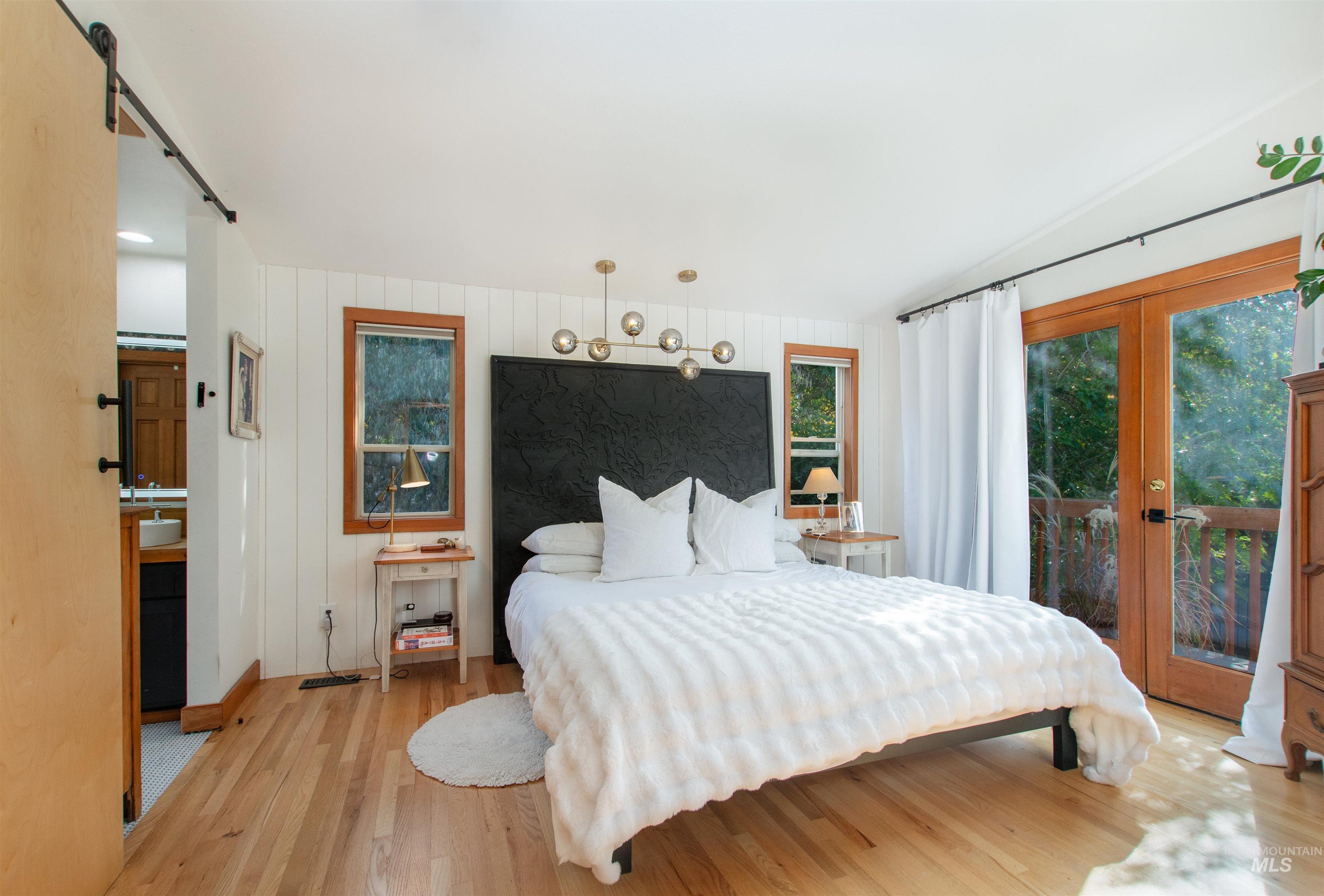 Bedroom featuring wood finished floors, wooden walls, access to outside, french doors, and a barn door
