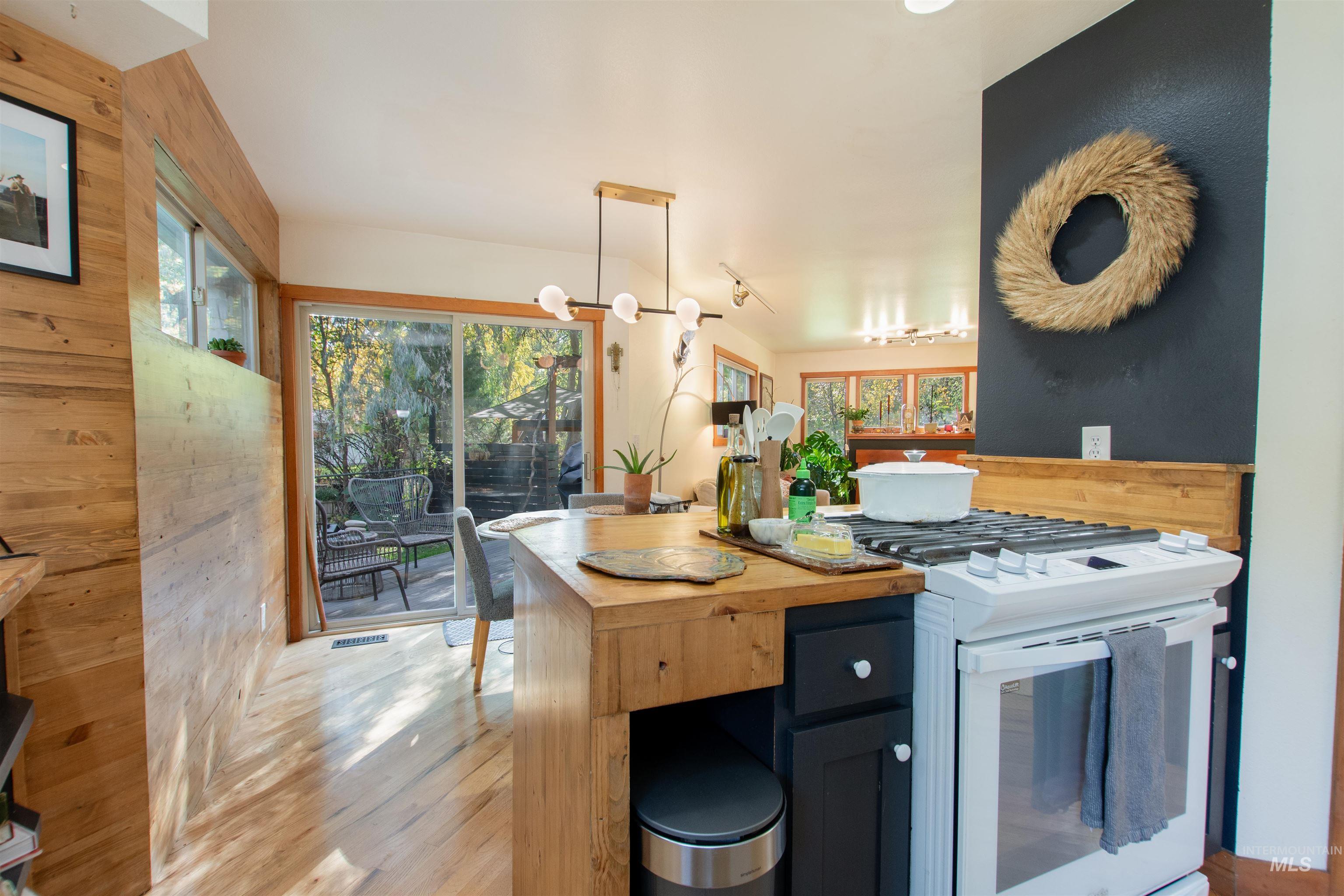 Kitchen with white range with gas stovetop, wood counters, hanging light fixtures, light wood-style flooring, and wooden walls