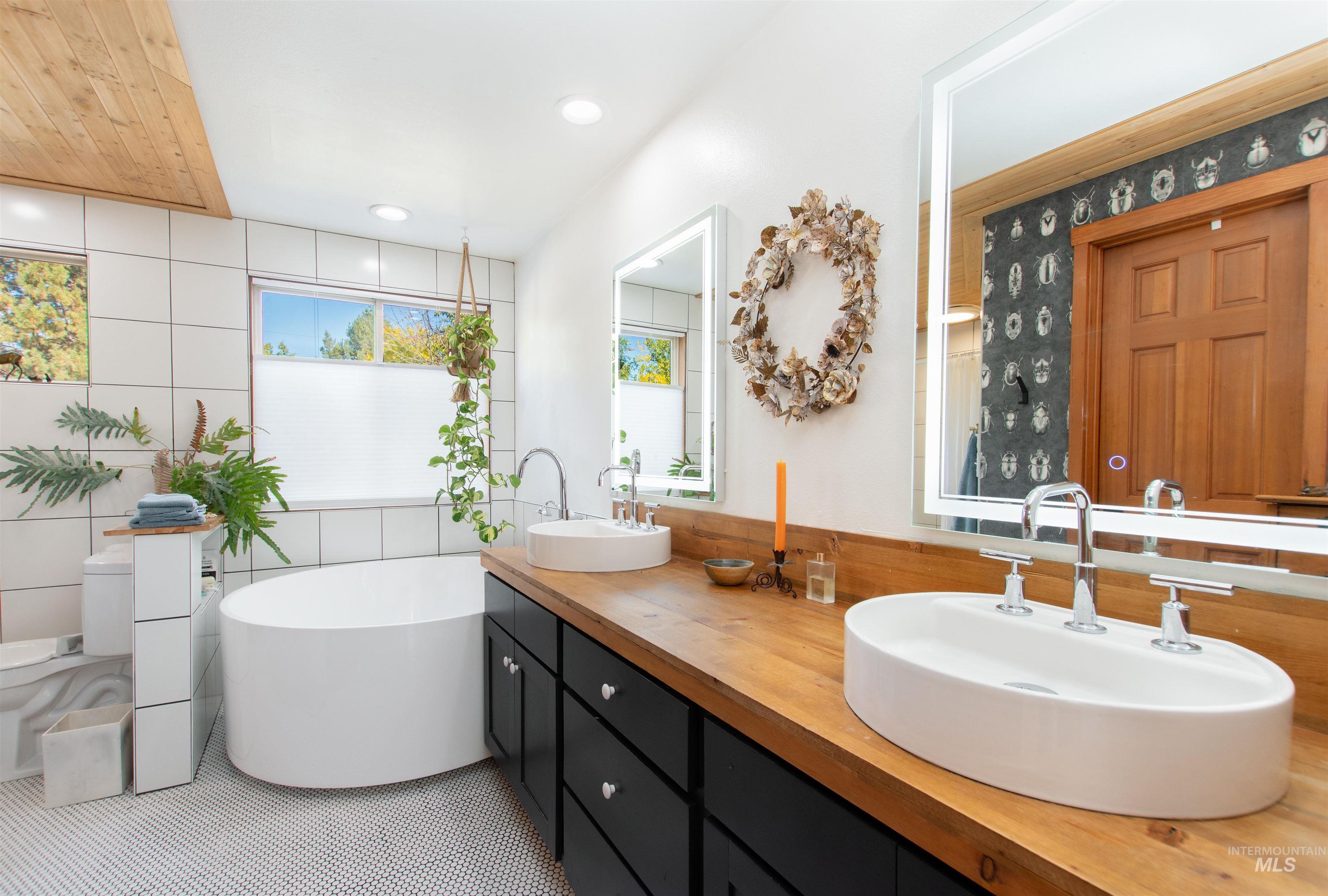 Full bath with double vanity, tile walls, a freestanding bath, recessed lighting, and tile patterned floors