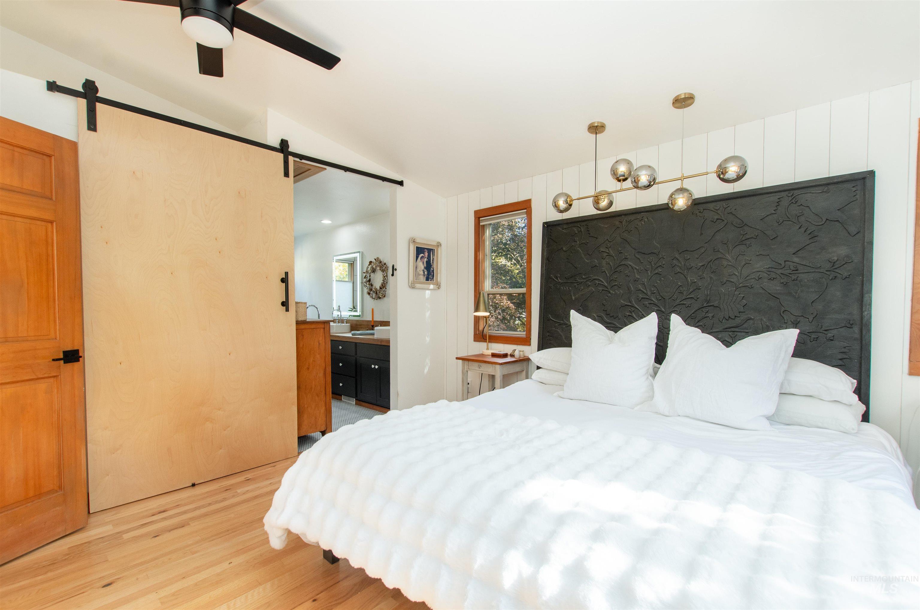 Bedroom with light wood-type flooring, lofted ceiling, a ceiling fan, a barn door, and a chandelier