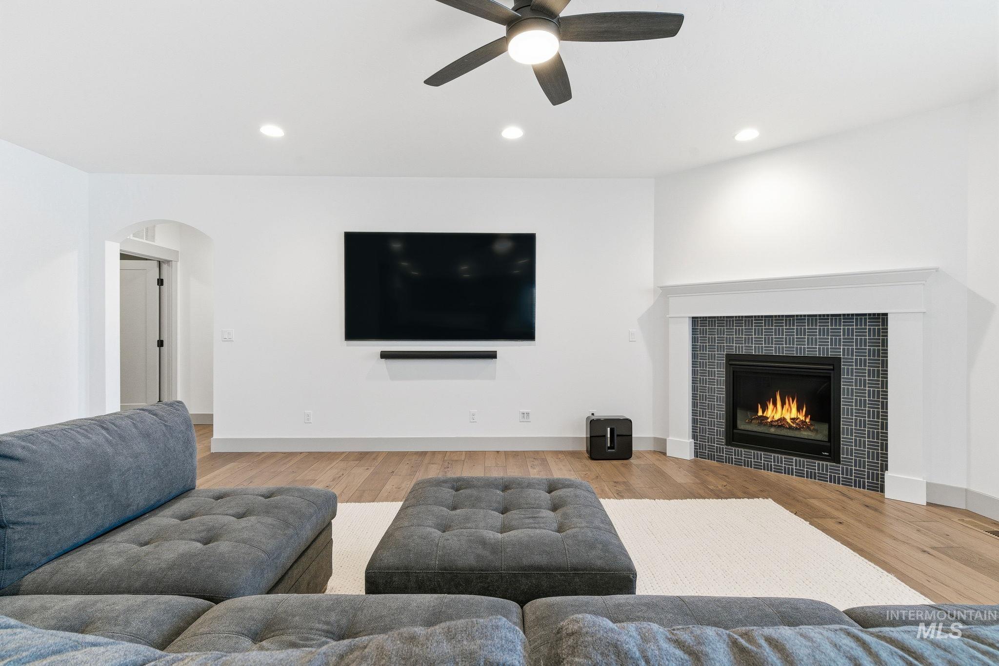 Living room featuring recessed lighting, light wood finished floors, a tiled fireplace, arched walkways, and a ceiling fan