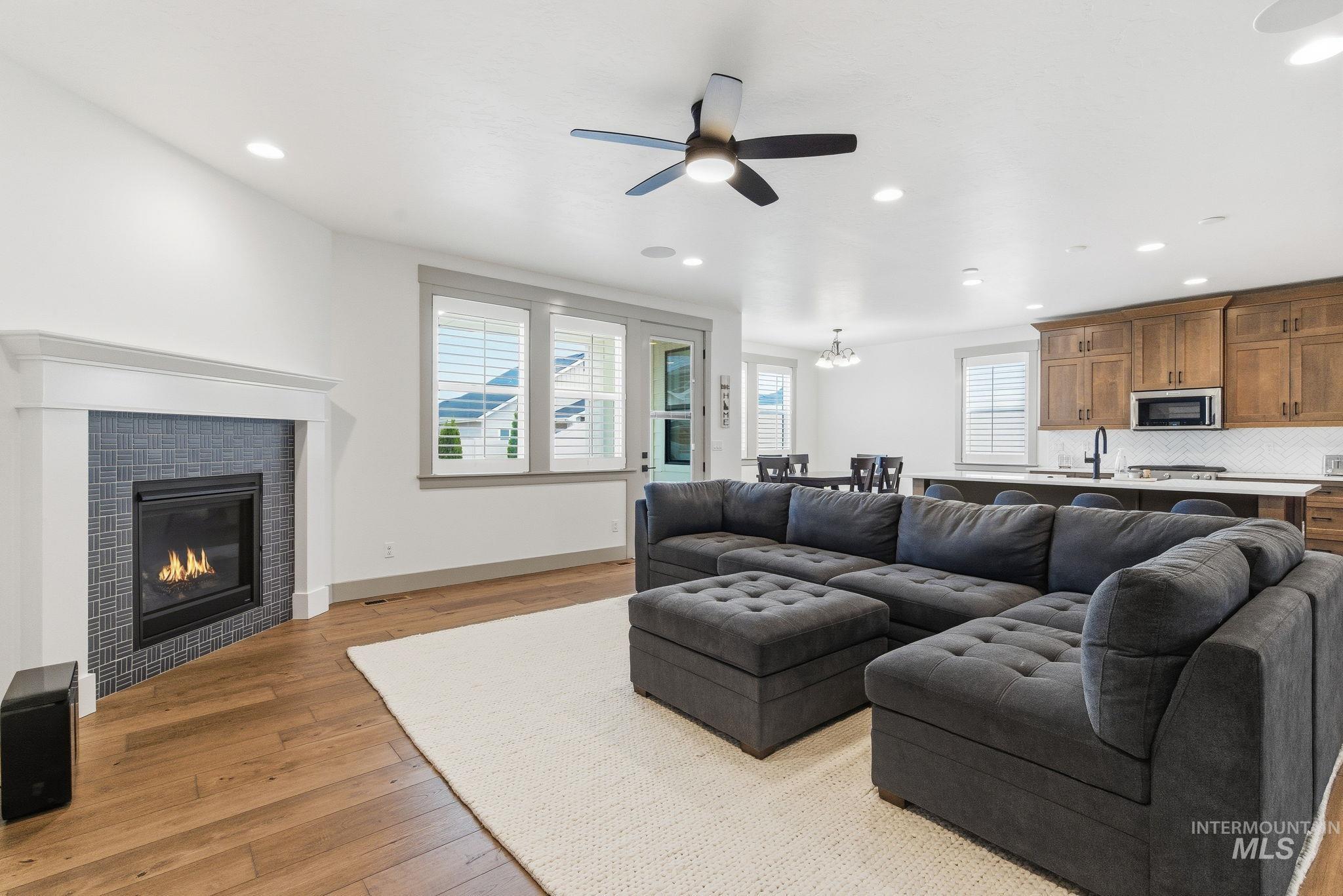 Living area with a tiled fireplace, recessed lighting, light wood-style flooring, and a ceiling fan