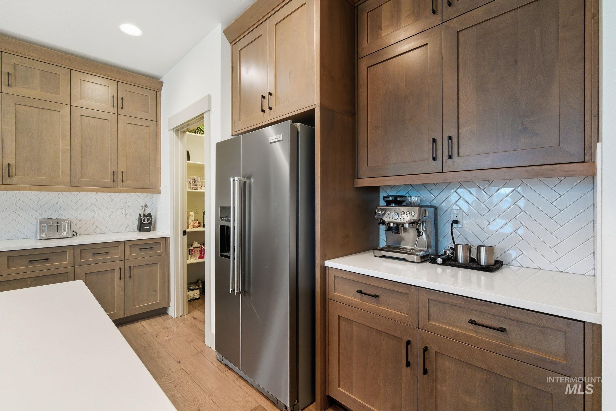 Kitchen with tasteful backsplash, high end refrigerator, brown cabinetry, light wood-type flooring, and light stone counters
