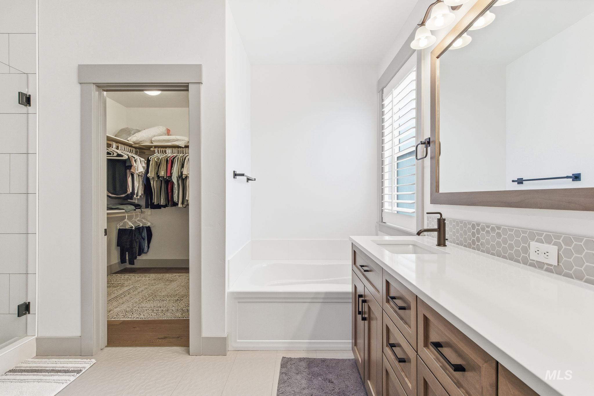 Bathroom featuring a walk in closet, vanity, light tile patterned flooring, and a garden tub