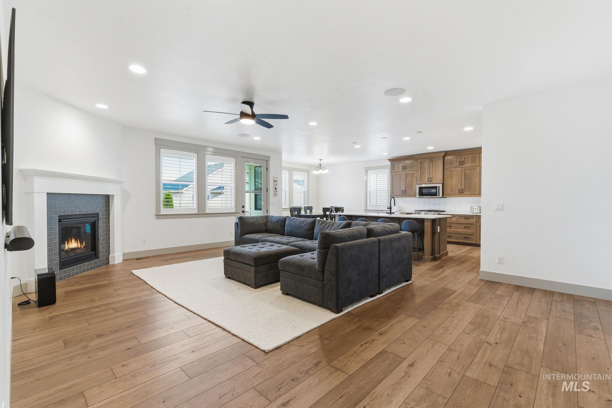 Living room with a glass covered fireplace, recessed lighting, light wood finished floors, ceiling fan, and a chandelier