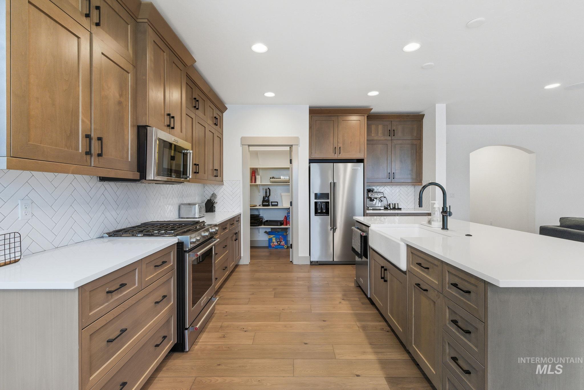 Kitchen with stainless steel appliances, brown cabinetry, tasteful backsplash, a kitchen island with sink, and recessed lighting