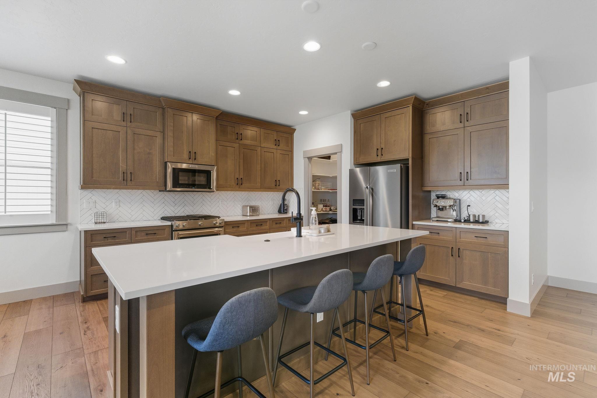 Kitchen featuring decorative backsplash, brown cabinets, high end appliances, light wood-style flooring, and recessed lighting