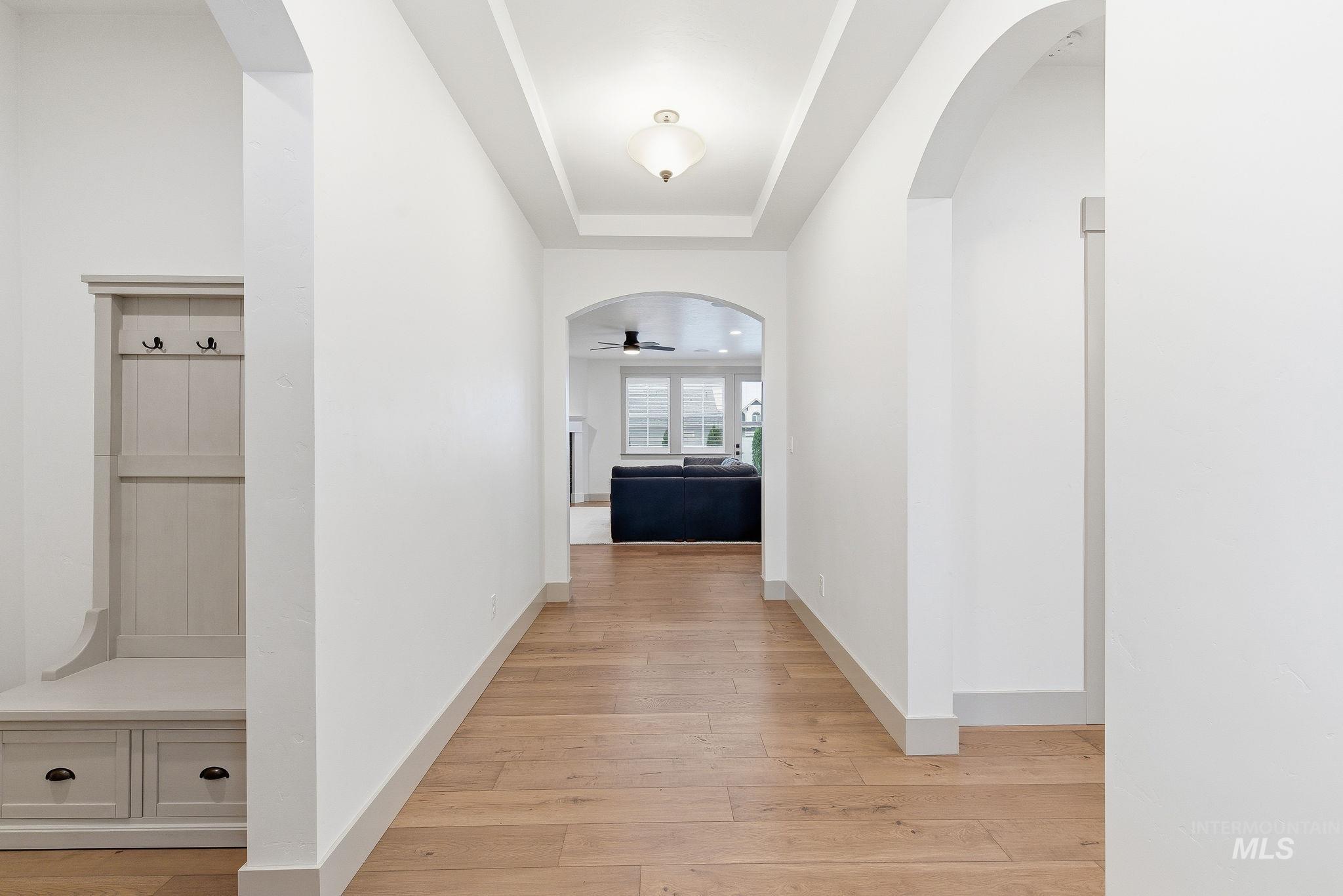 Corridor featuring arched walkways, light wood-style flooring, and a tray ceiling
