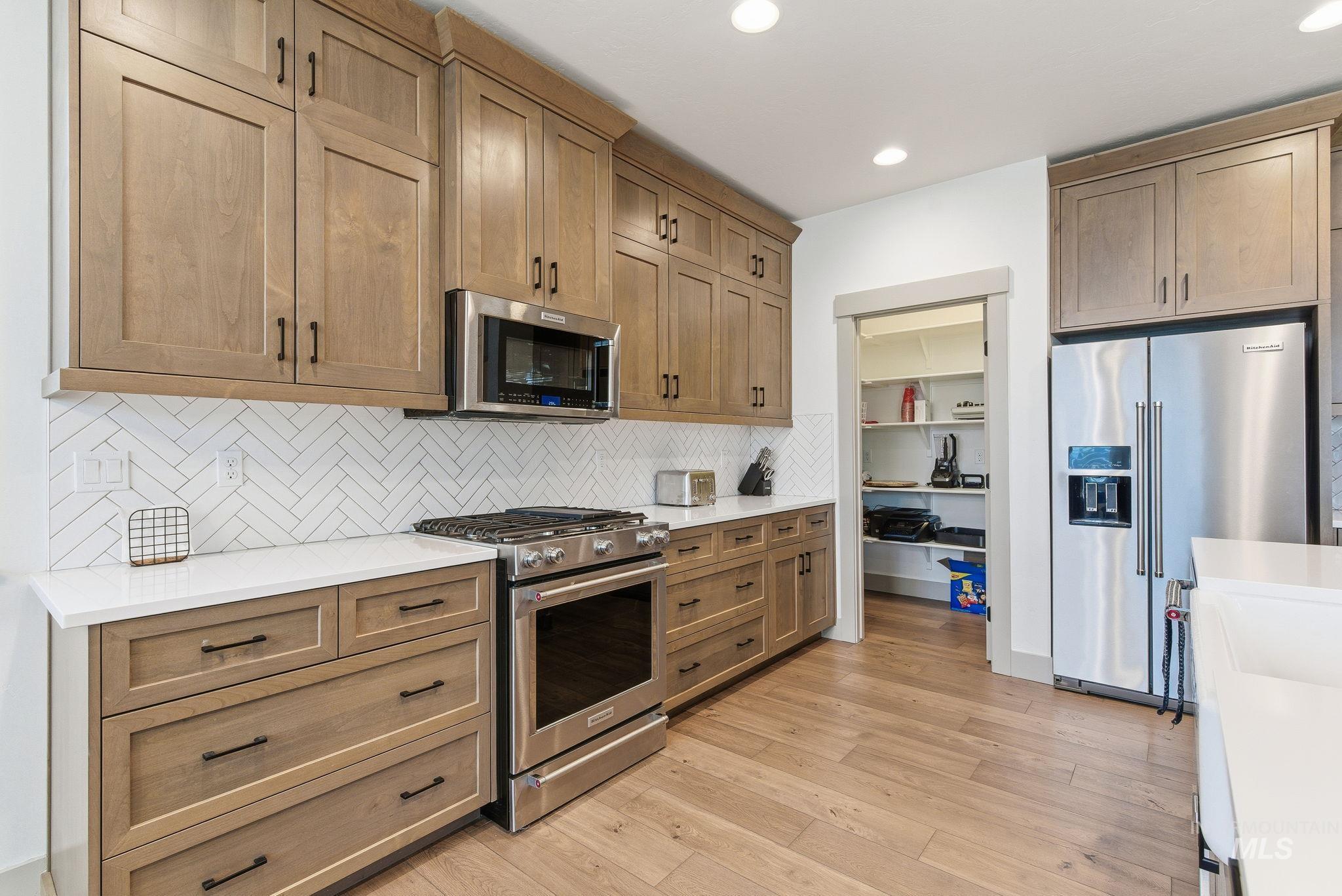 Kitchen with stainless steel appliances, decorative backsplash, brown cabinetry, light wood-type flooring, and recessed lighting