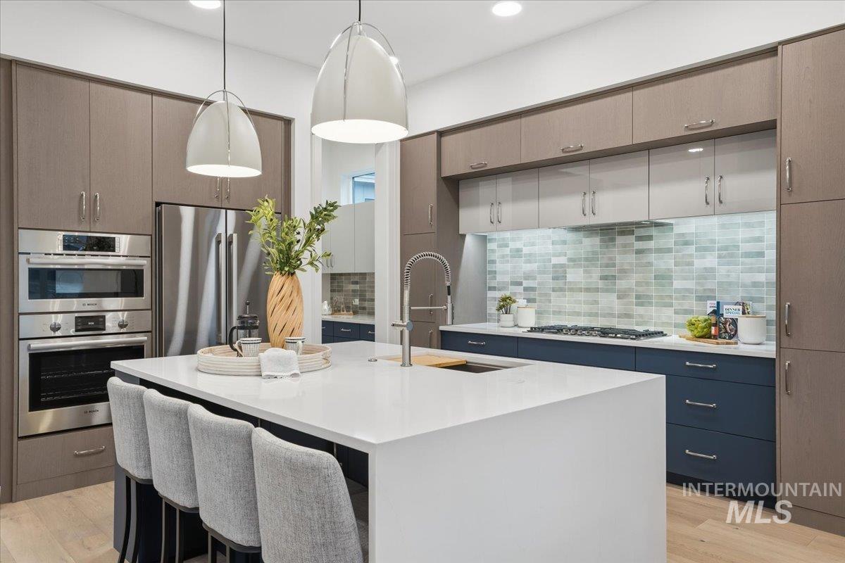 Kitchen with hanging light fixtures, tasteful backsplash, a breakfast bar, stainless steel appliances, and a kitchen island with sink