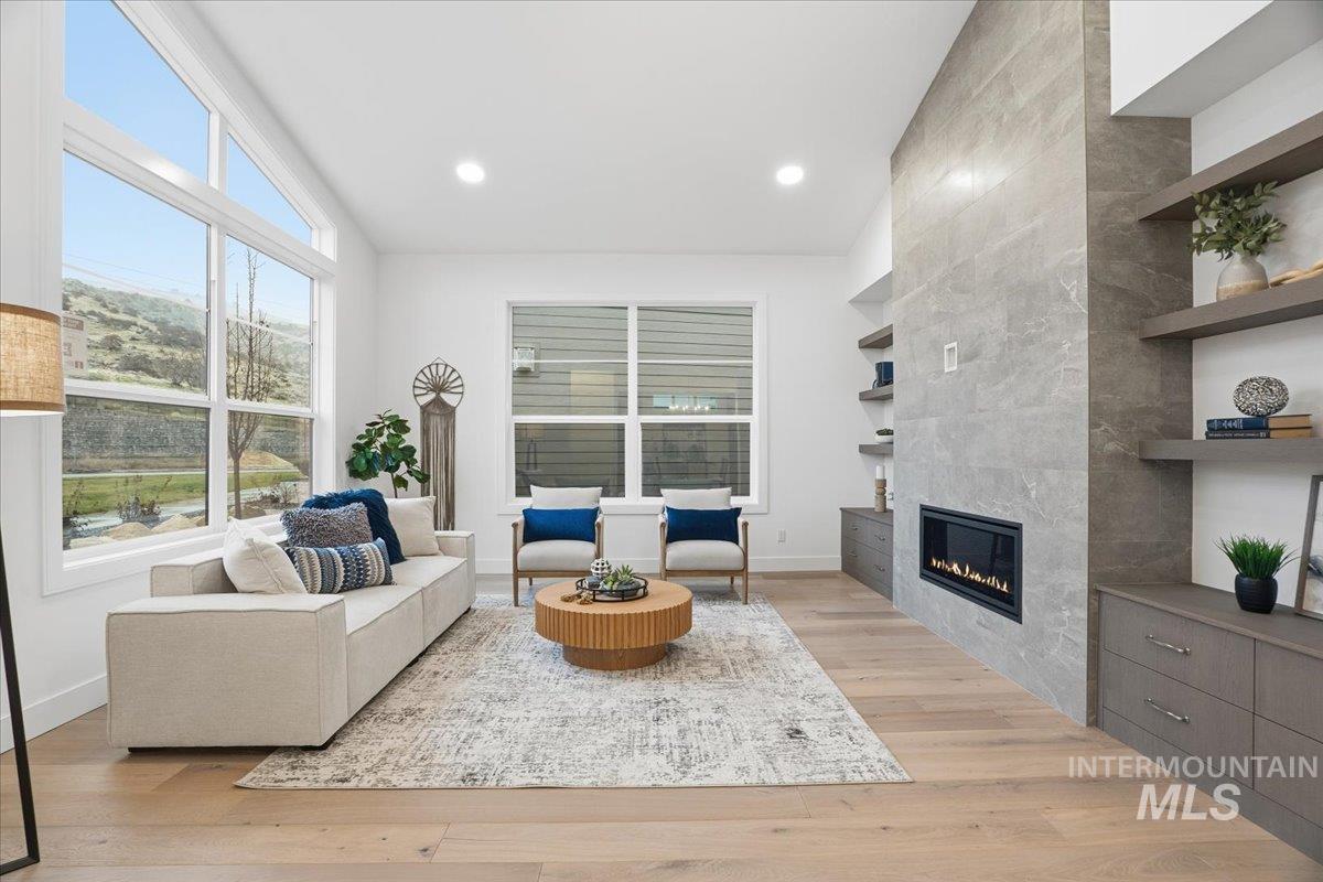 Living room featuring light wood finished floors, a tiled fireplace, plenty of natural light, and recessed lighting