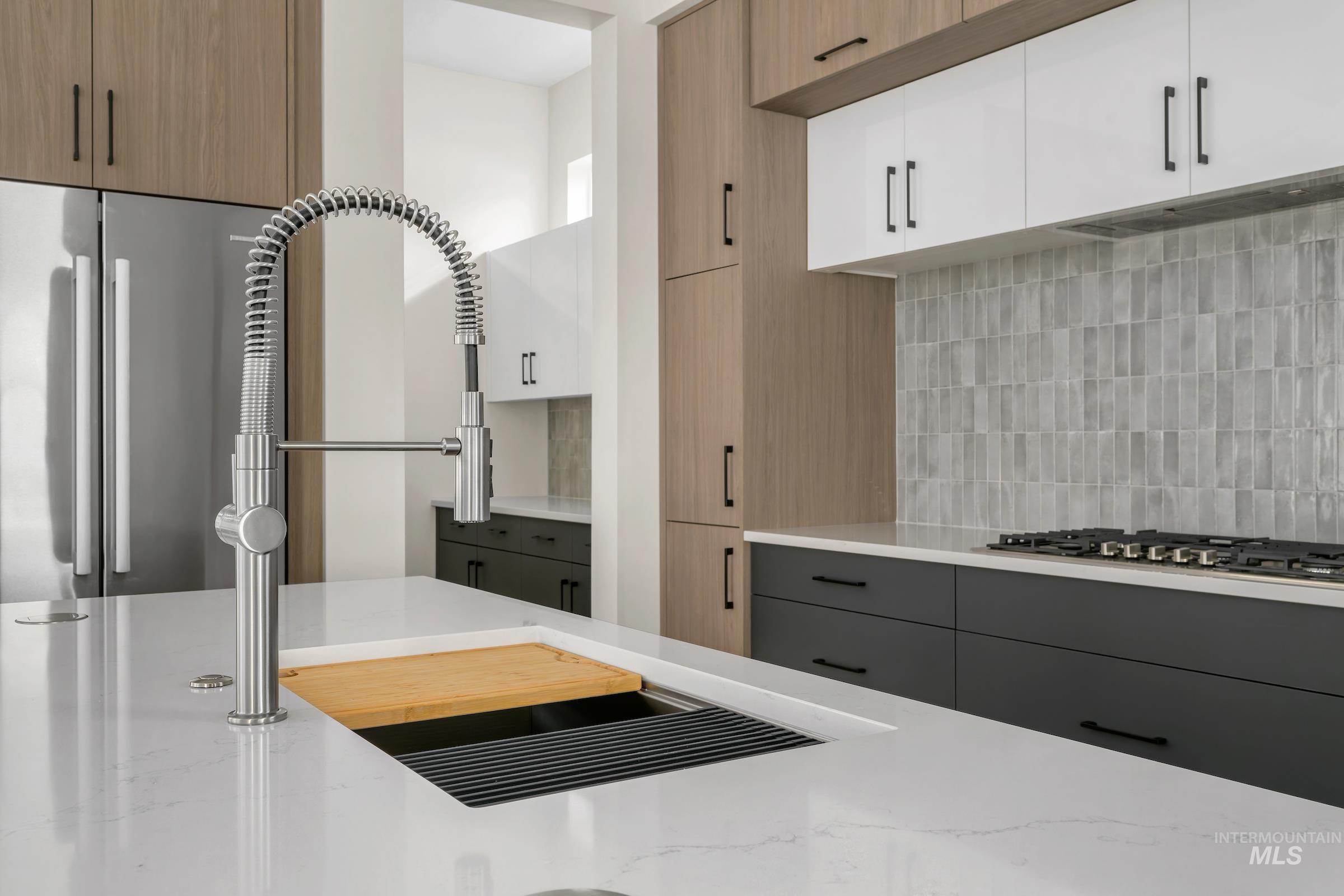 Kitchen with white cabinets, appliances with stainless steel finishes, backsplash, light stone counters, and modern cabinets