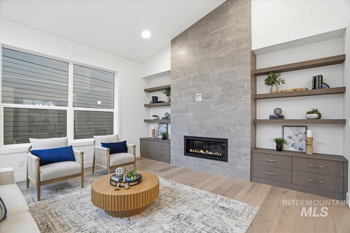 Living area featuring built in shelves, vaulted ceiling, light wood-style flooring, and a tile fireplace
