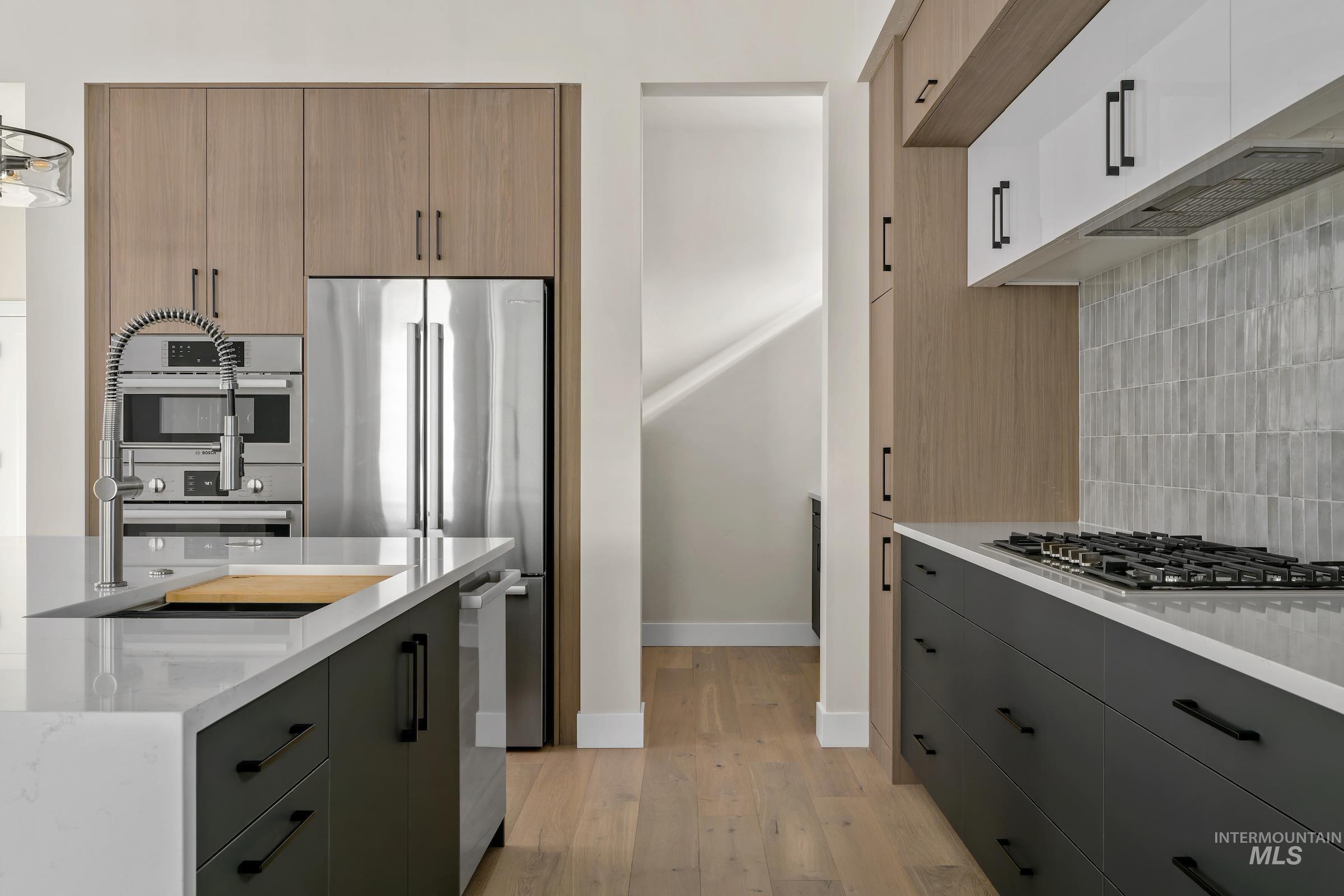 Kitchen with light wood-type flooring, light stone counters, stainless steel appliances, backsplash, and modern cabinets